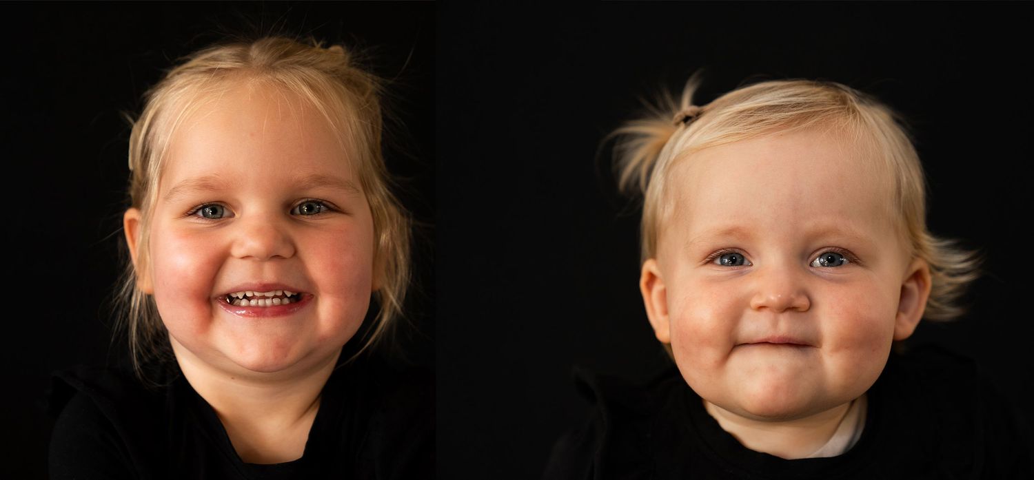 Portret van twee lachende blonde peuters naast elkaar tegen een zwarte achtergrond.
