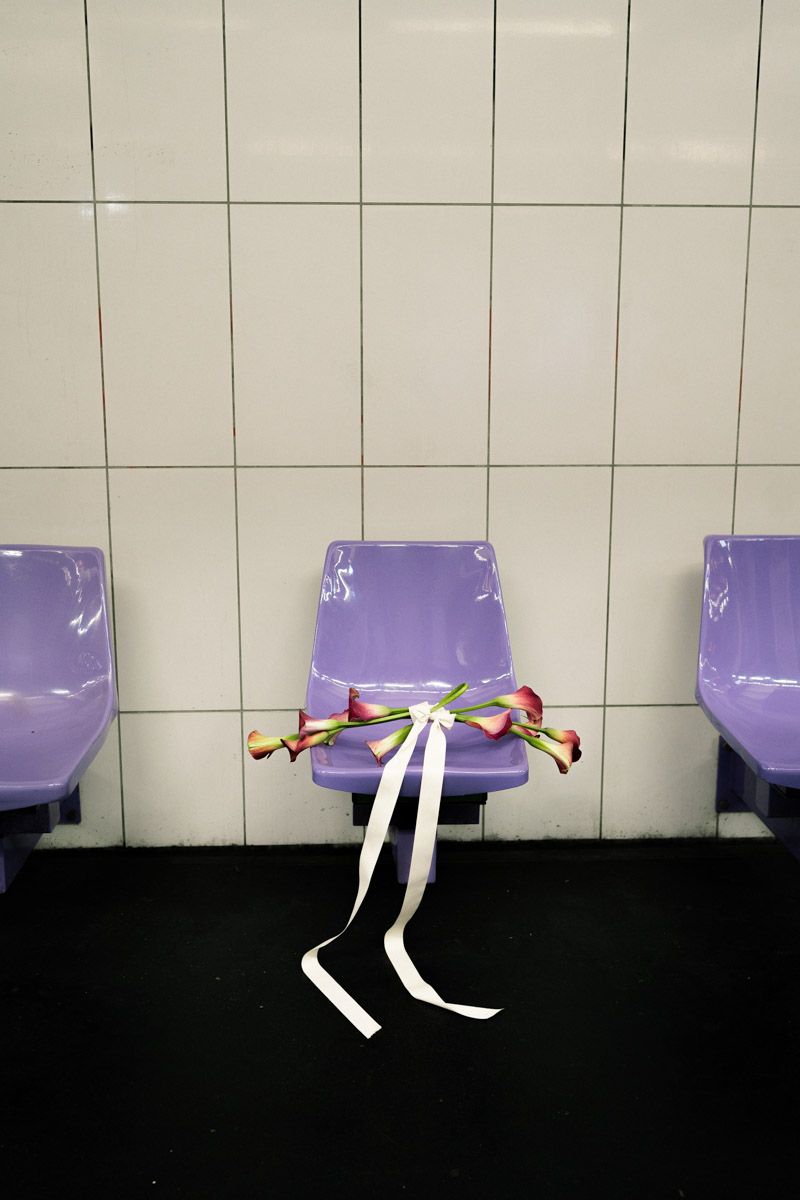 Purple plastic chairs against white tiled wall with calla lilies tied with white ribbon on center seat.