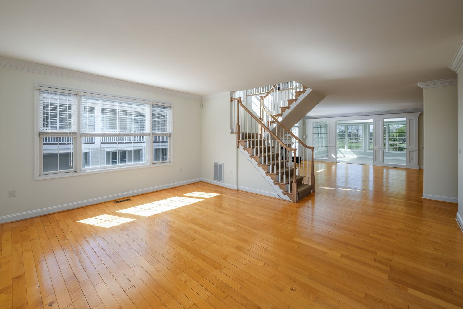 Bright open living room with hardwood floors, white walls, staircase, and large windows letting in natural light.
