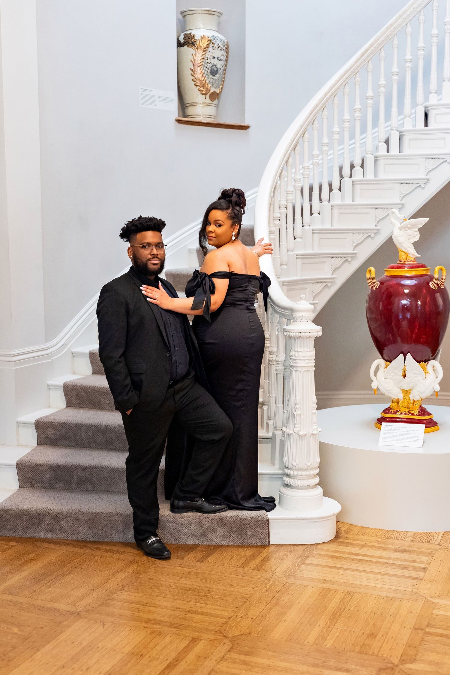 Elegant couple in formal attire pose in an ornate hallway with yellow walls and marble columns.