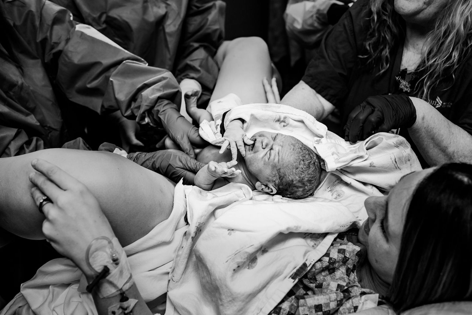 Black and white photograph of medical professionals attending to a newborn baby wrapped in white cloth.