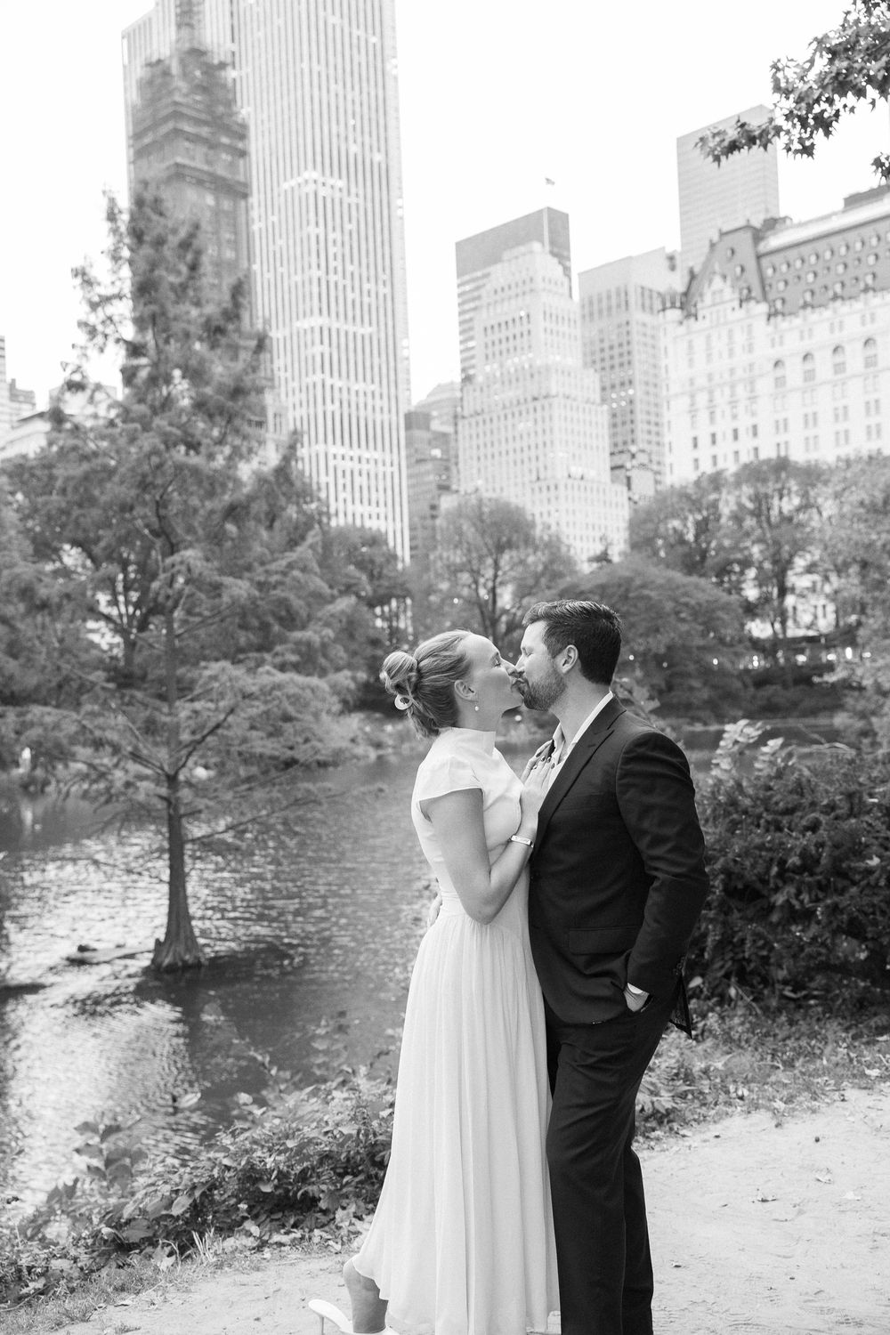 Bride and groom kissing in Central Park with Manhattan skyscrapers in the background.