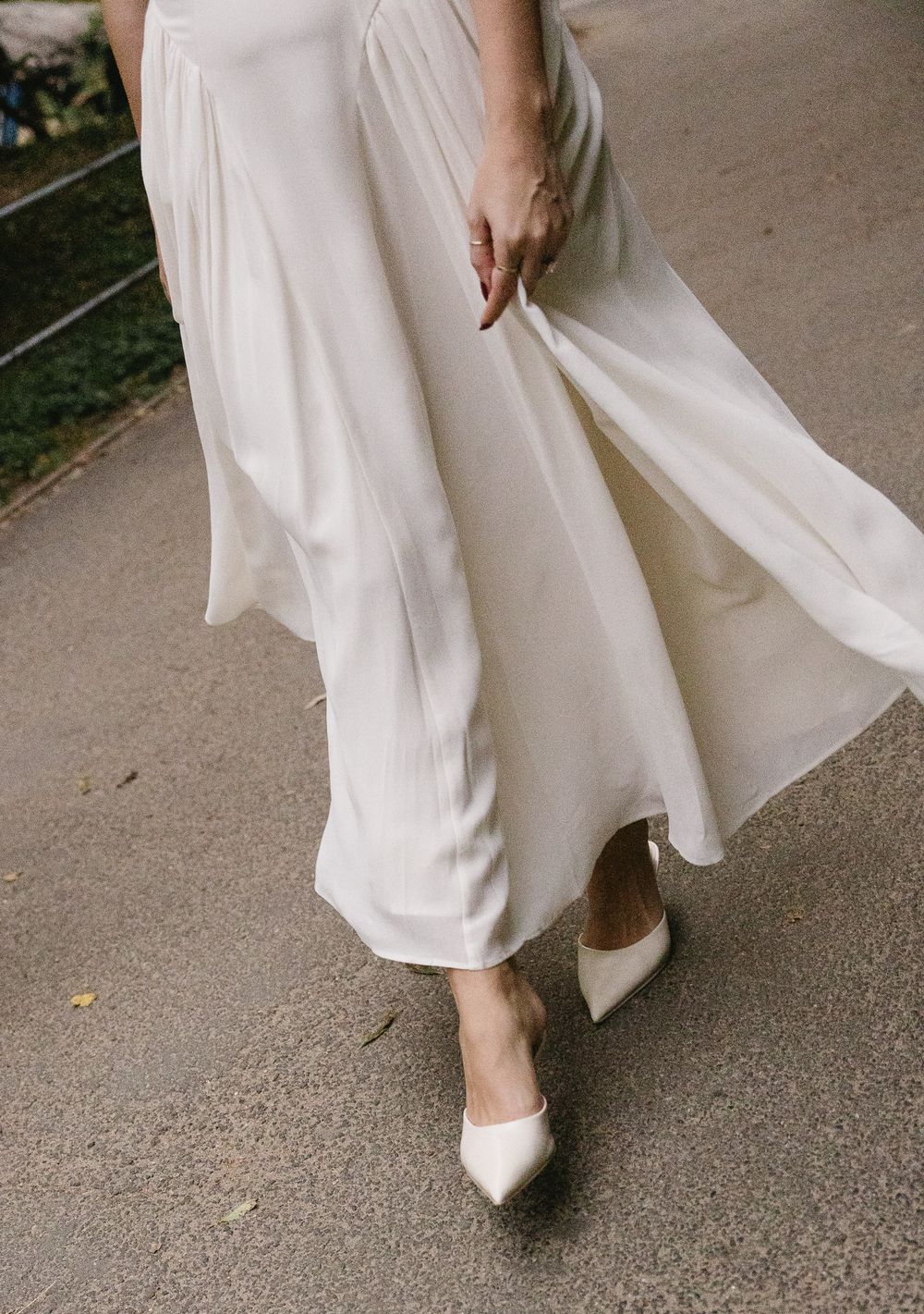 Close-up of a bride walking in ivory pointed-toe heels with a flowing white satin wedding skirt.