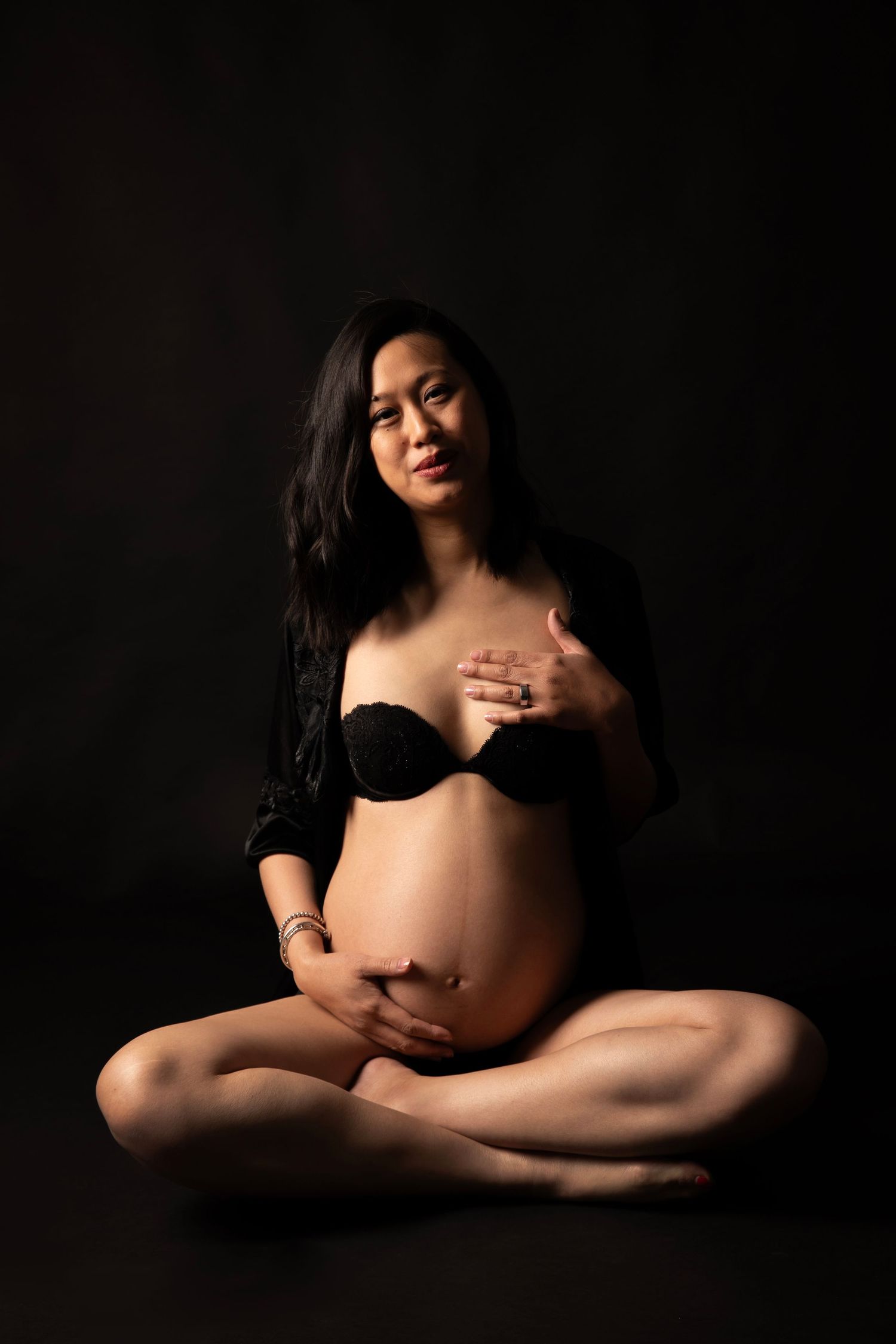 Black and white portrait of expectant mother in dark dress touching her baby bump.