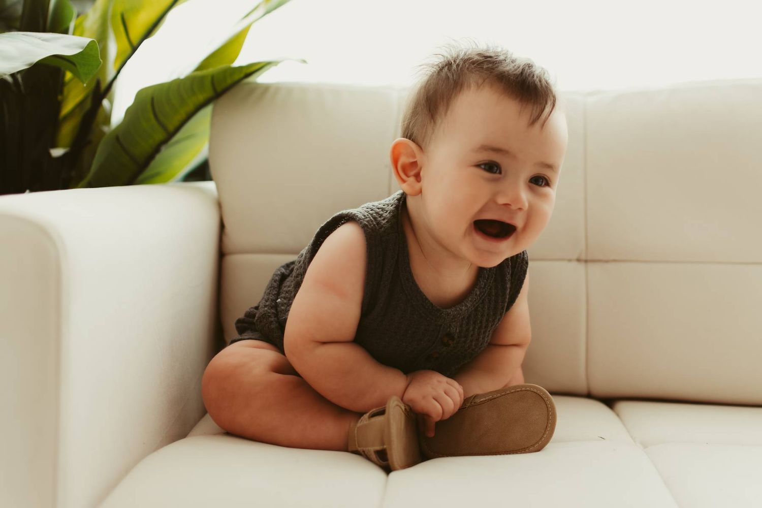 Baby lying on white couch with green plant in background.