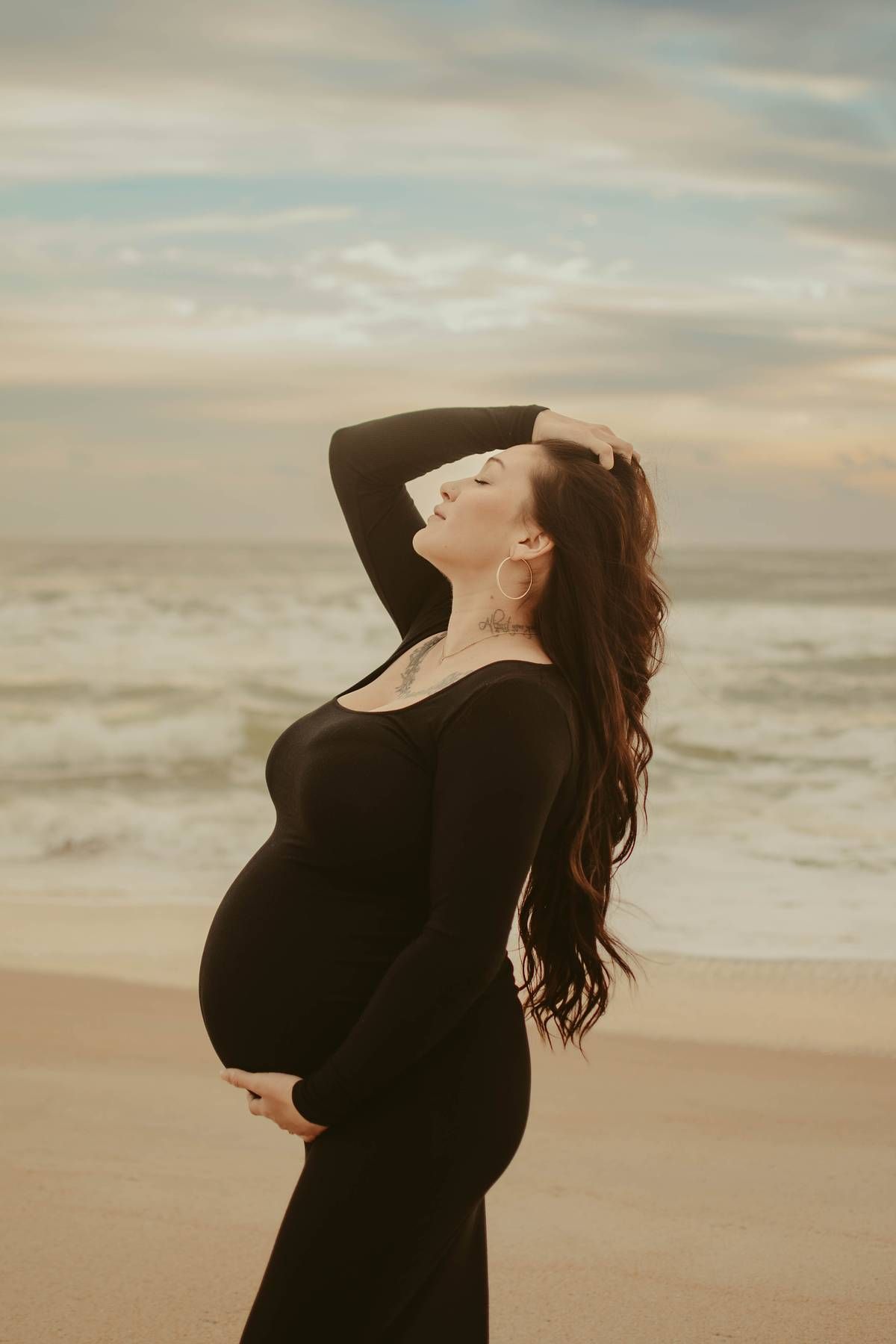 Silhouette of a person in black dress dancing on beach at sunset.