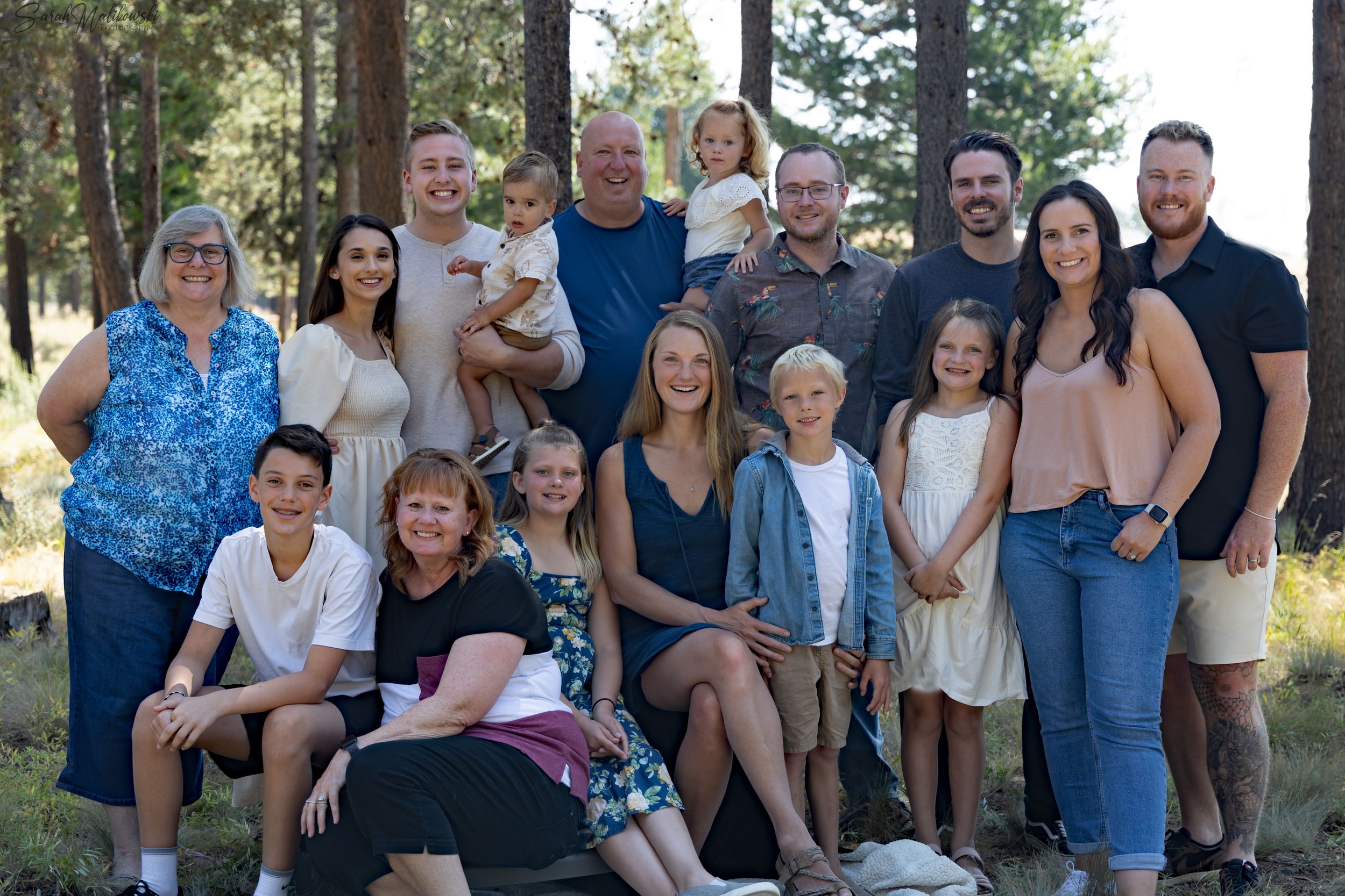 Extended family gathering for group photos in a sunny wooded area.