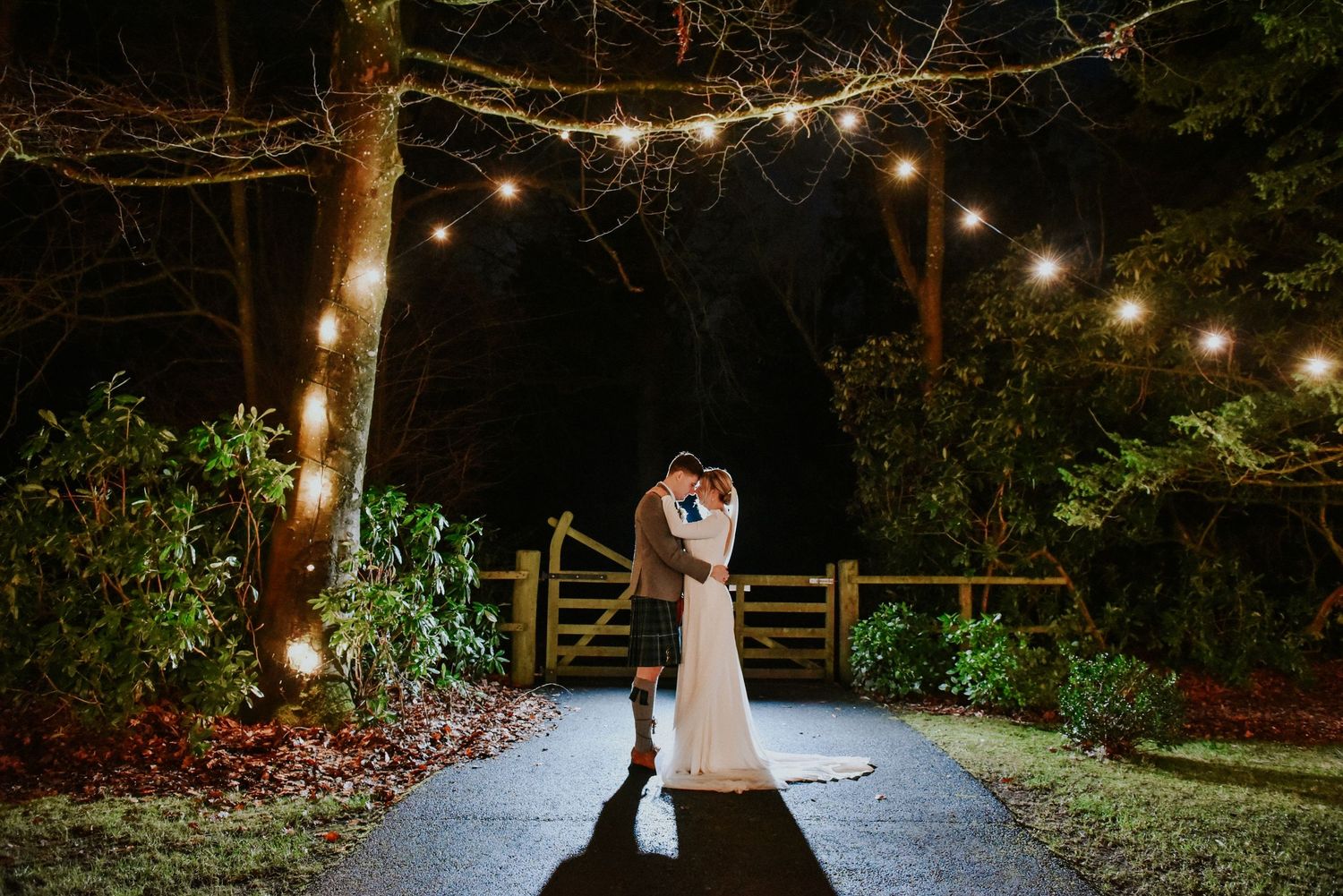 Bride and Groom  sharing a kiss while holding floral bouquet.and under fairy lights at Boswell Estate Ayrshire