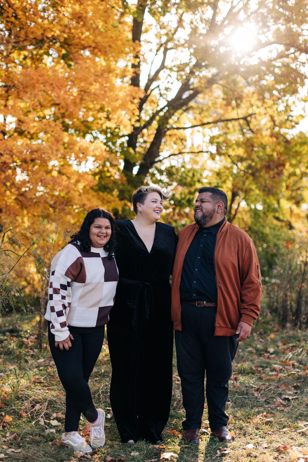 A group stands together outdoors on an autumn day with golden leaves and sunlight streaming through the trees.