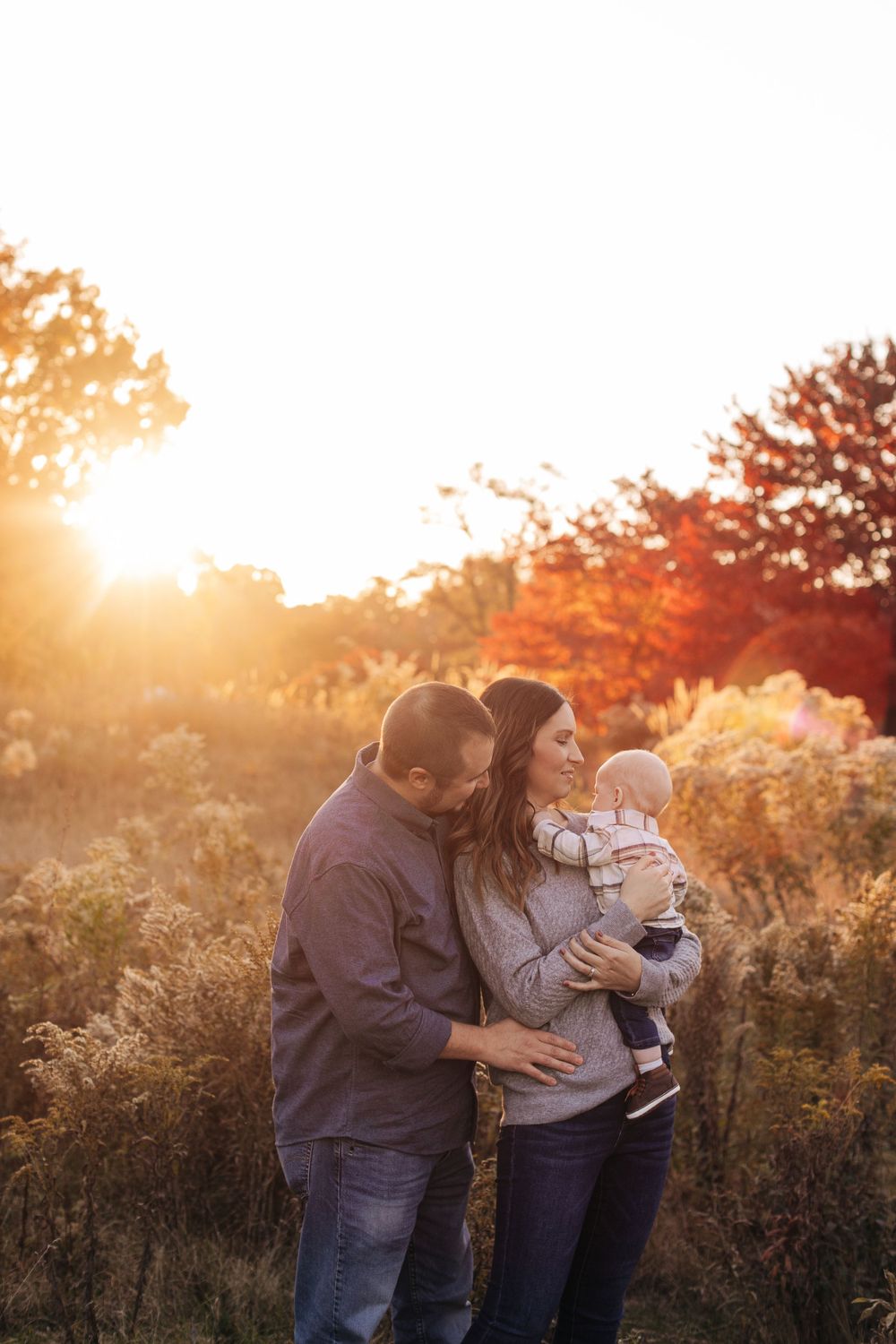 A family enjoys quality time together in a field during sunset with autumn colors in the background.