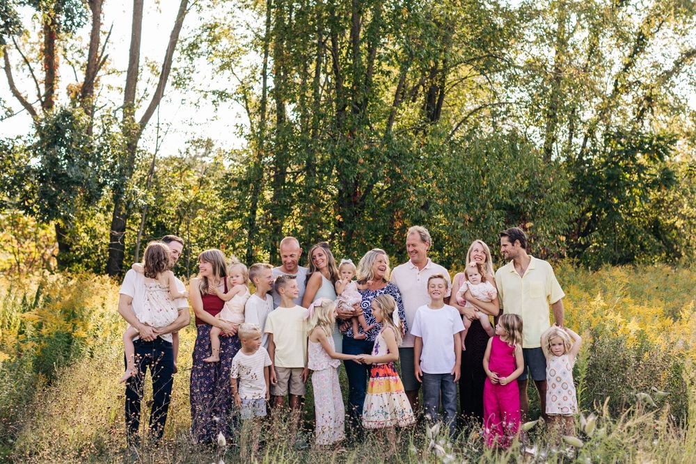 A large group poses together for a family portrait in a sunlit field with trees in the background.