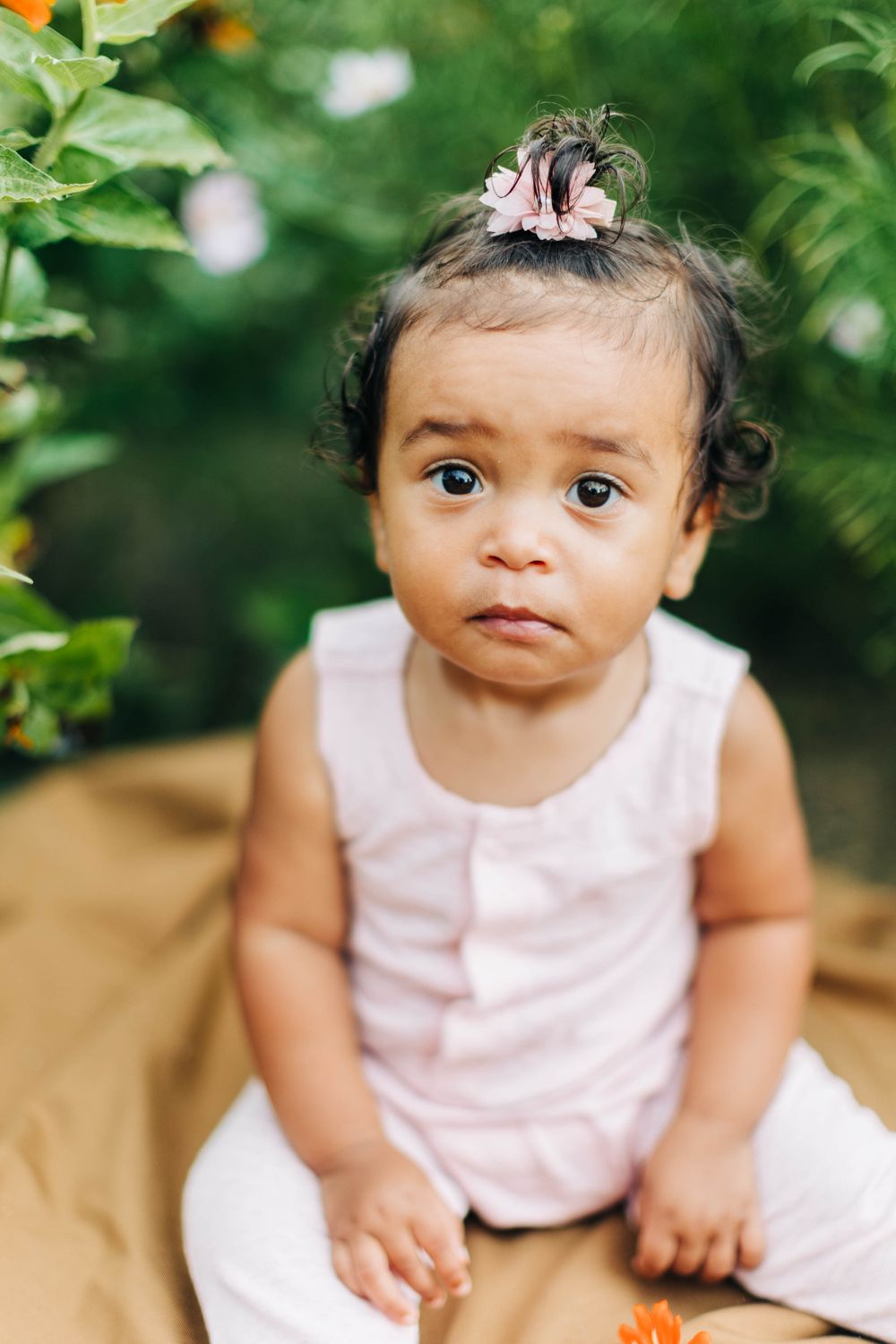 Toddler in pink dress sitting outdoors with curious expression.