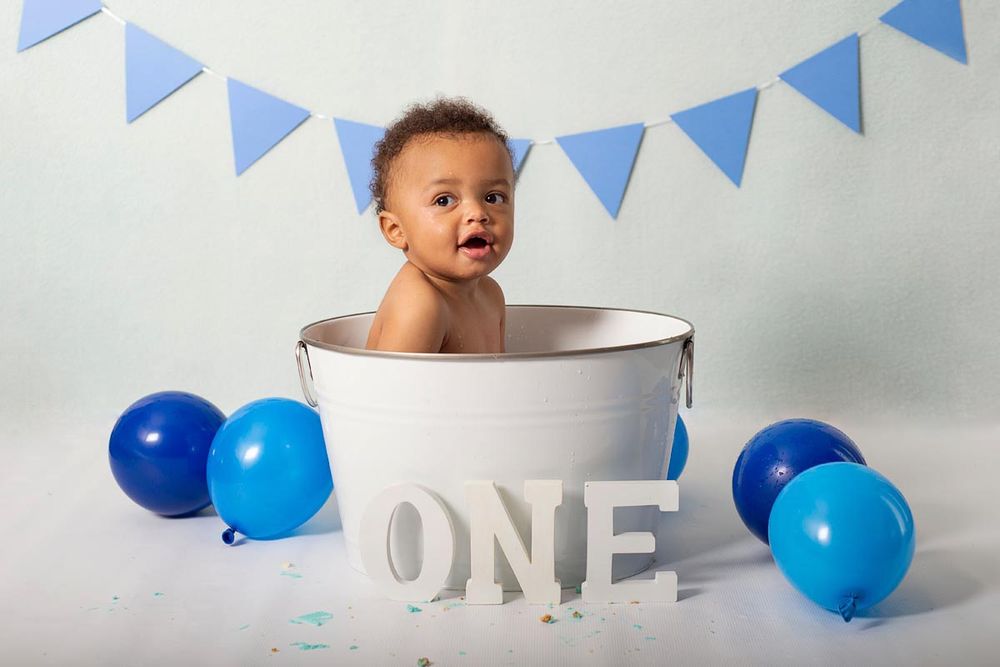 one year old boy sits in little white bathtub for his first birthday cake smash session in studio*