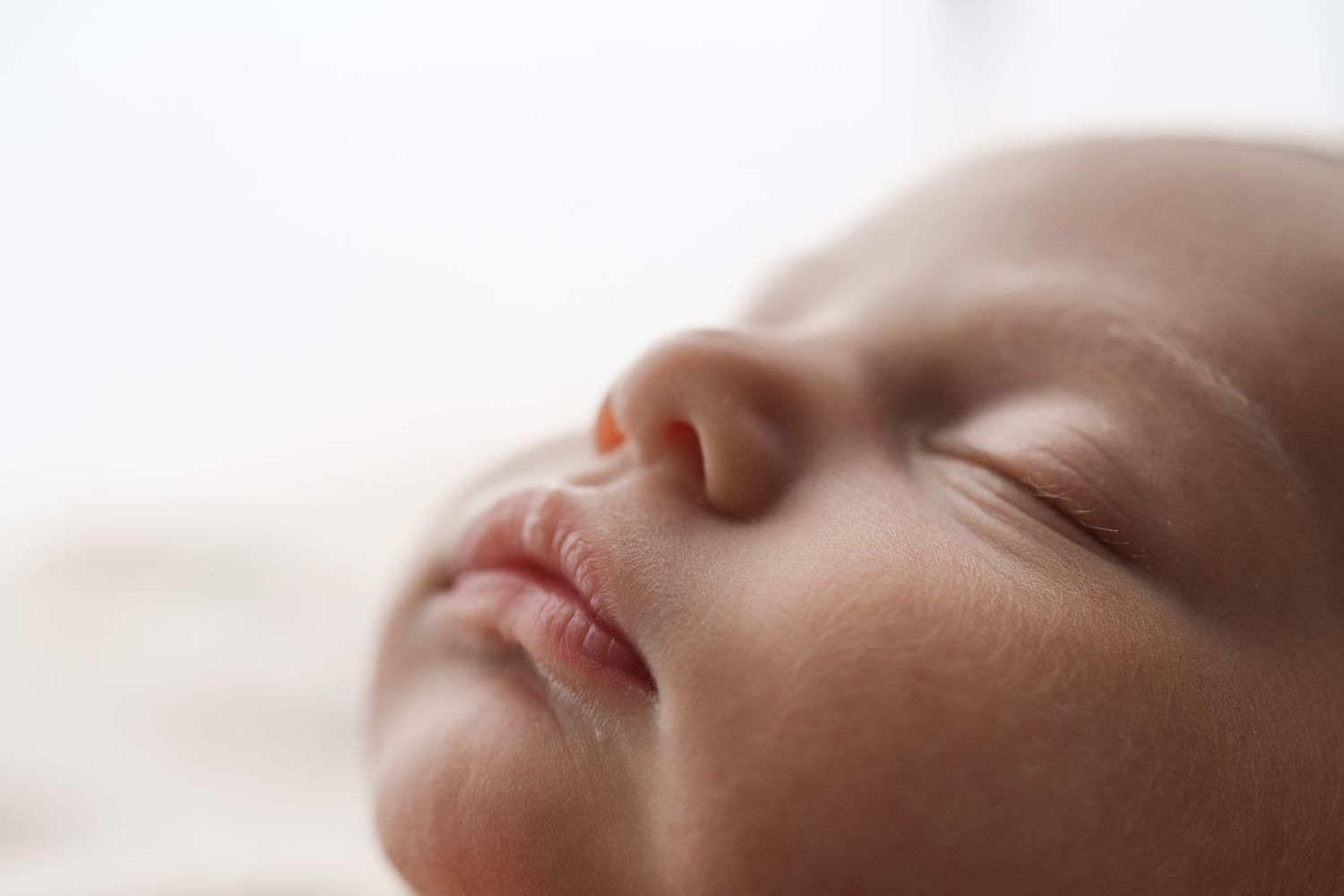 Adorable sleeping newborn poses with hands on chin on a colorful quilt in a miniature bed.