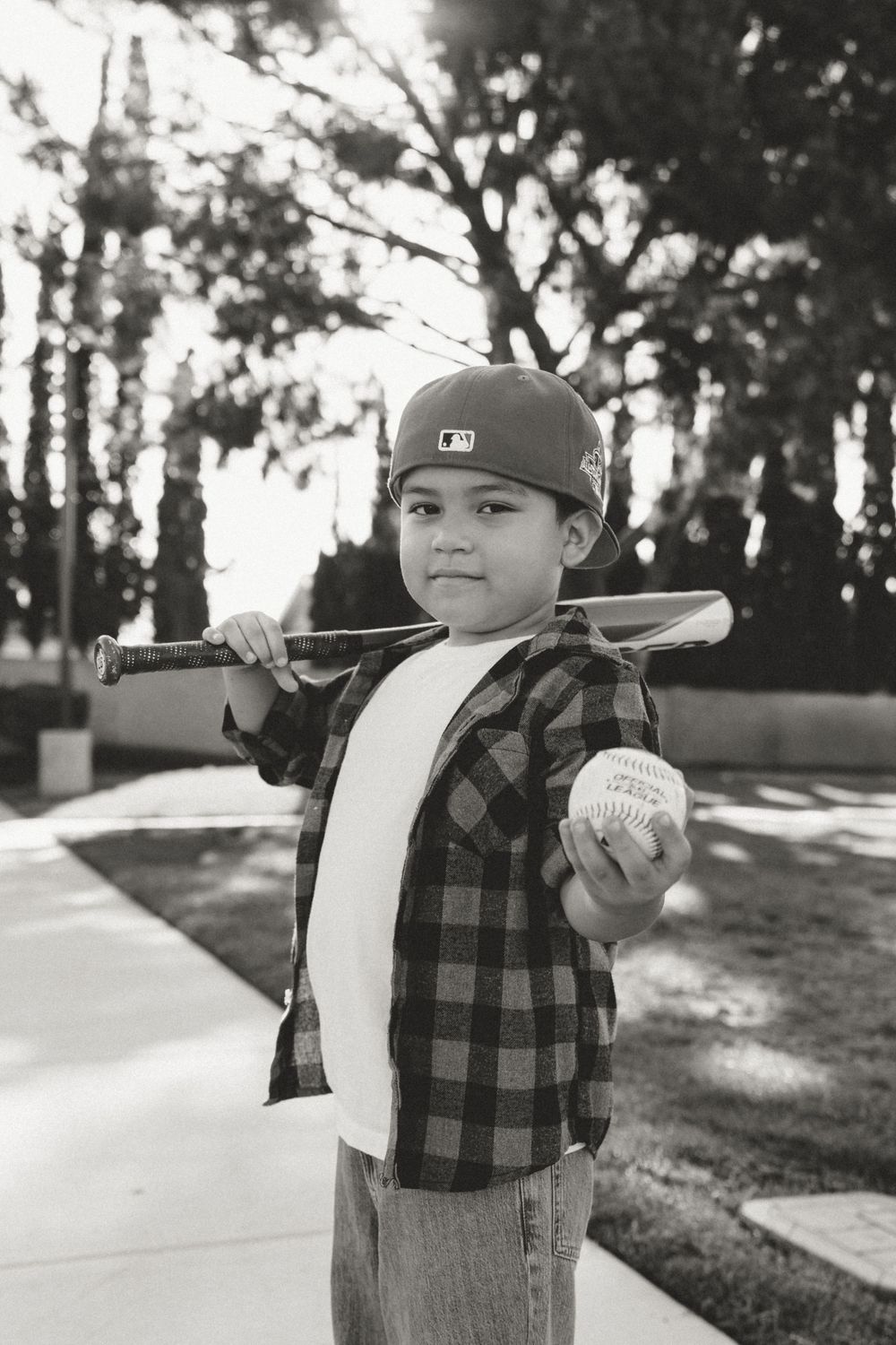 Black and white photo series of a young child in plaid and baseball cap posing outdoors.