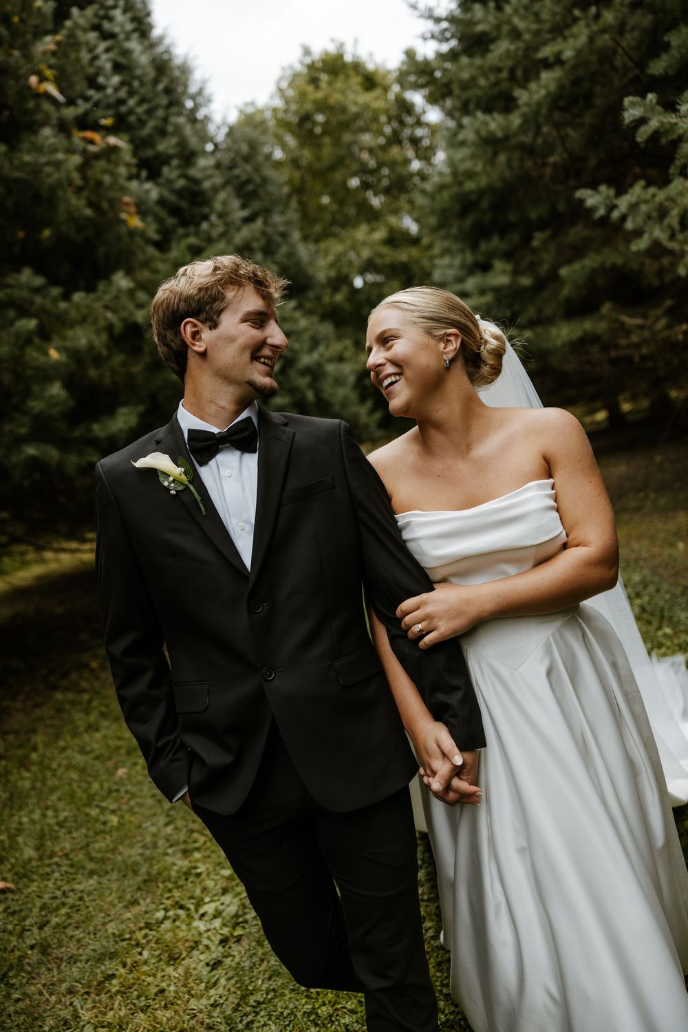 A happy couple, a bride in a white dress and a groom in a black suit, walking together in a lush, wooded setting. Fort Worth Texas.