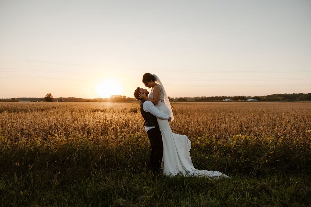 A bride and groom embrace in a golden field at sunset, creating a romantic and picturesque scene. Fort Worth Texas wedding photographer.