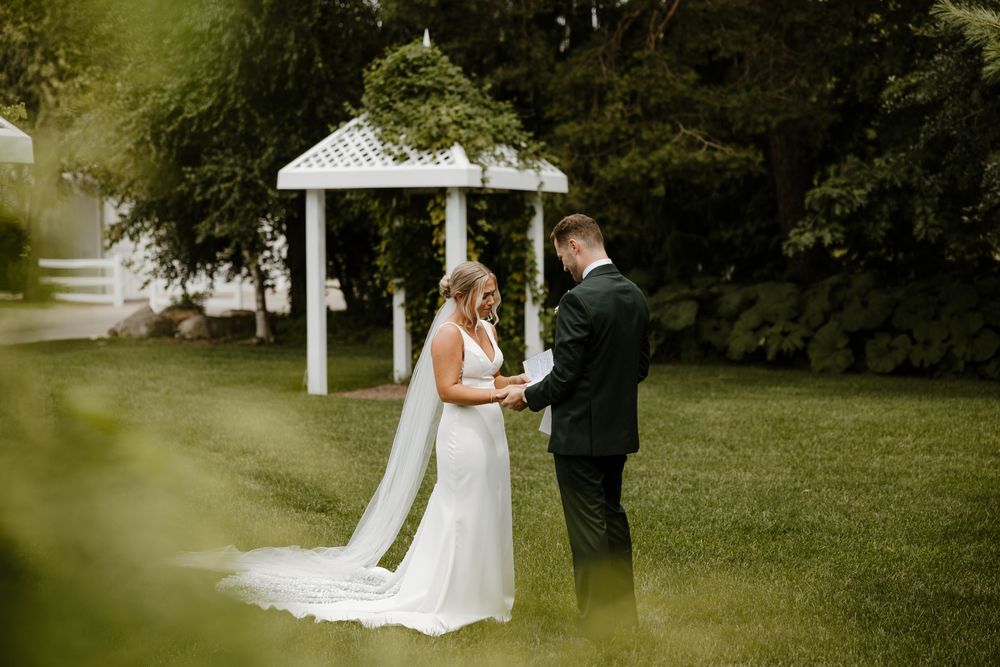 A bride and groom embrace in a garden setting with a white gazebo in the background. Fort Worth Texas wedding photographer.