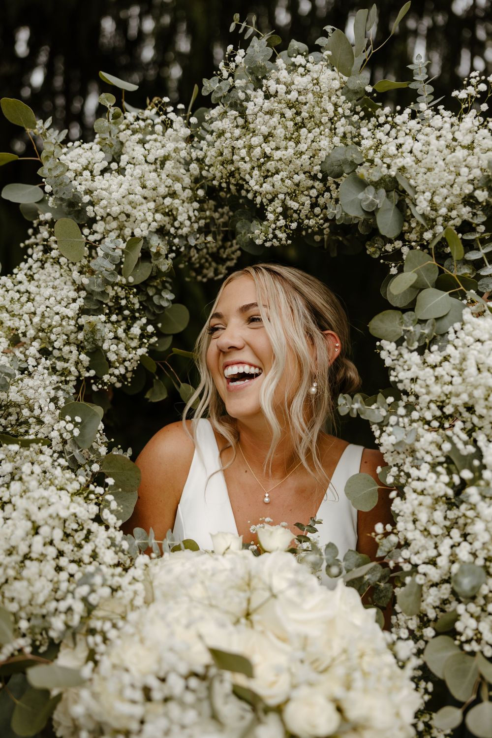 A smiling woman surrounded by a lush floral arrangement of white flowers. Fort Worth Texas wedding photographer.