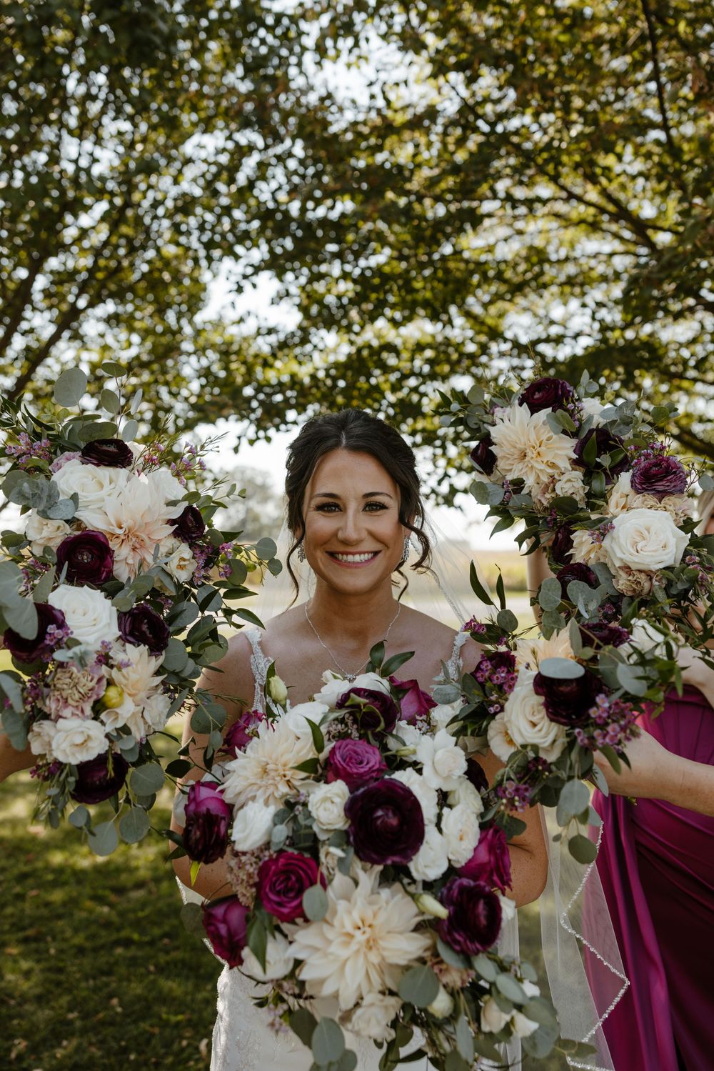 A smiling woman wearing a white wedding dress stands among vibrant floral arrangements in an outdoor setting. Fort Worth Texas photographer.