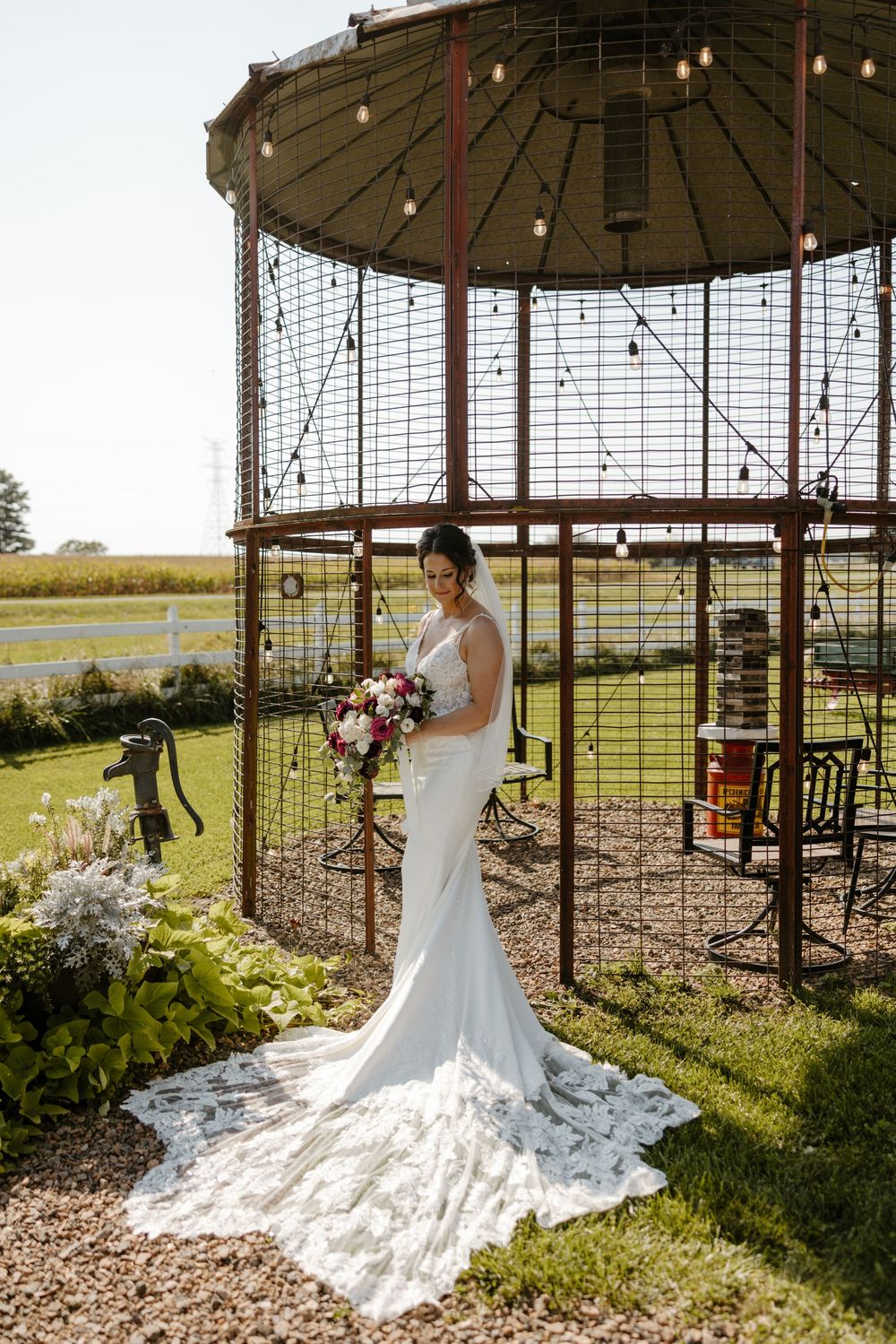 A bride stands in a rustic gazebo surrounded by lush greenery and flowers on her wedding day. Fort Worth Texas wedding photographer.