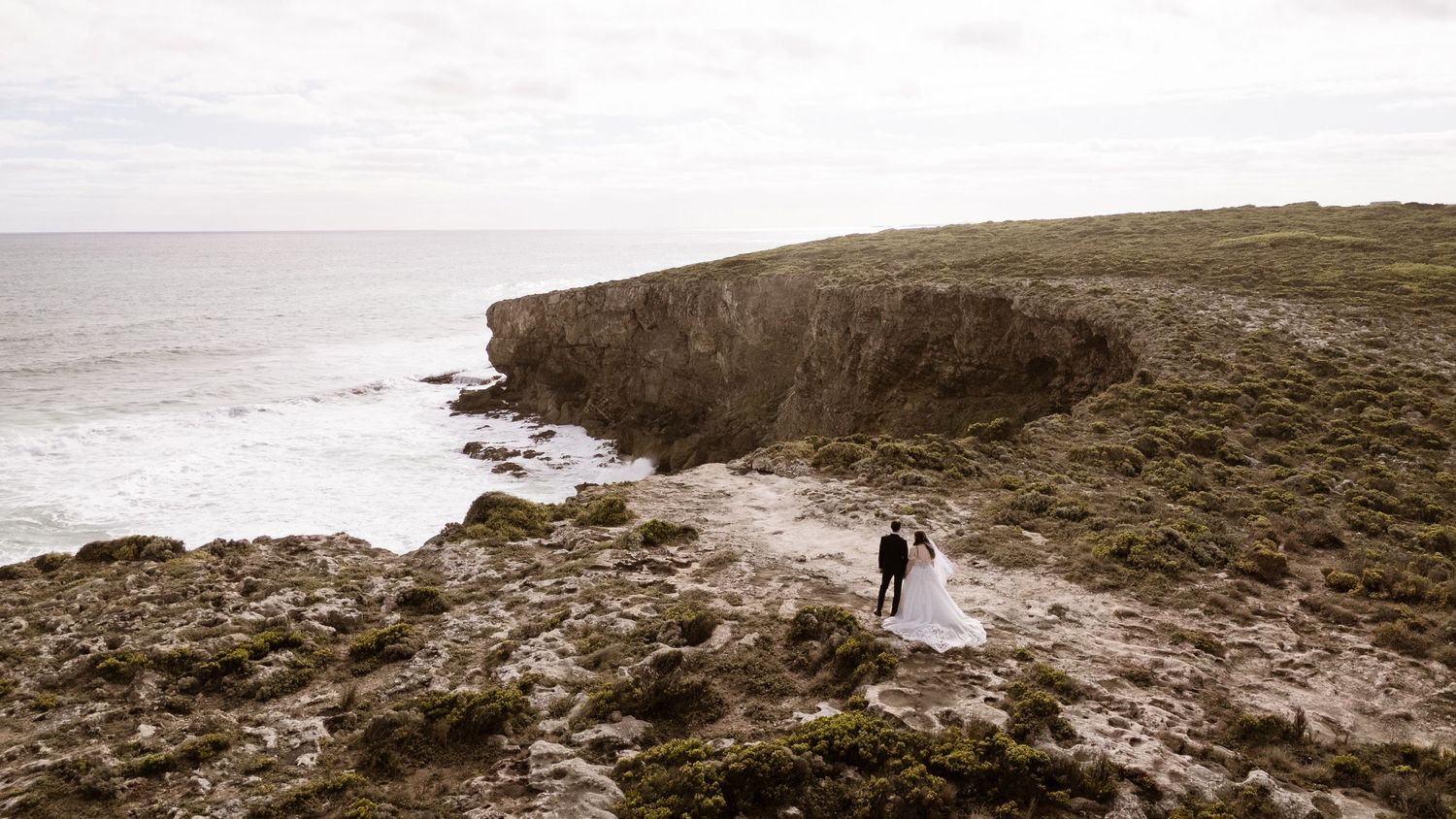 Panoramic view of a rocky coastline with distant figures walking along the shore.