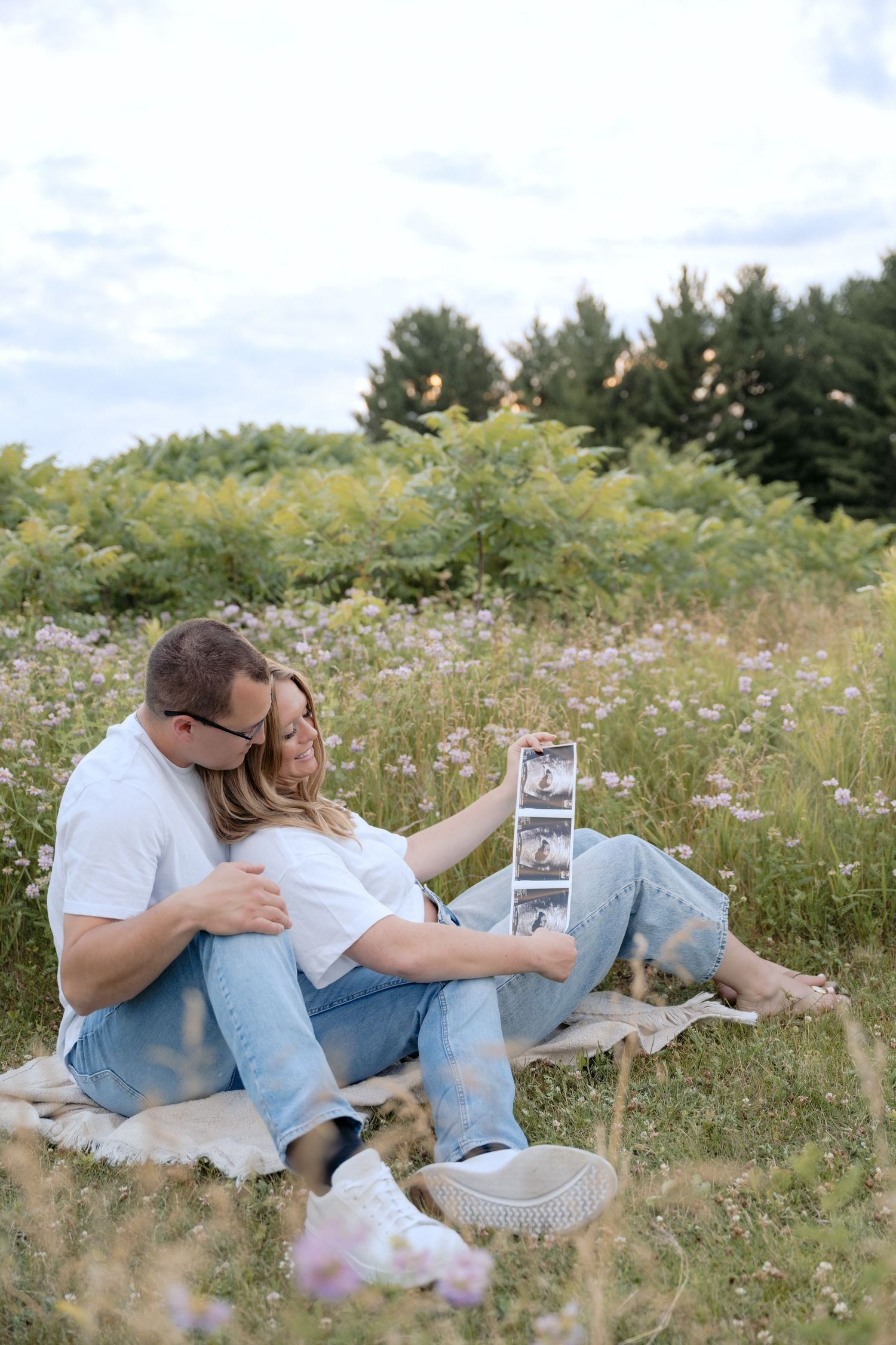 newly pregnant couple looking at ultrasound photos during outdoor field pregnancy announcement portraits in hudson wi with jagger rose photo