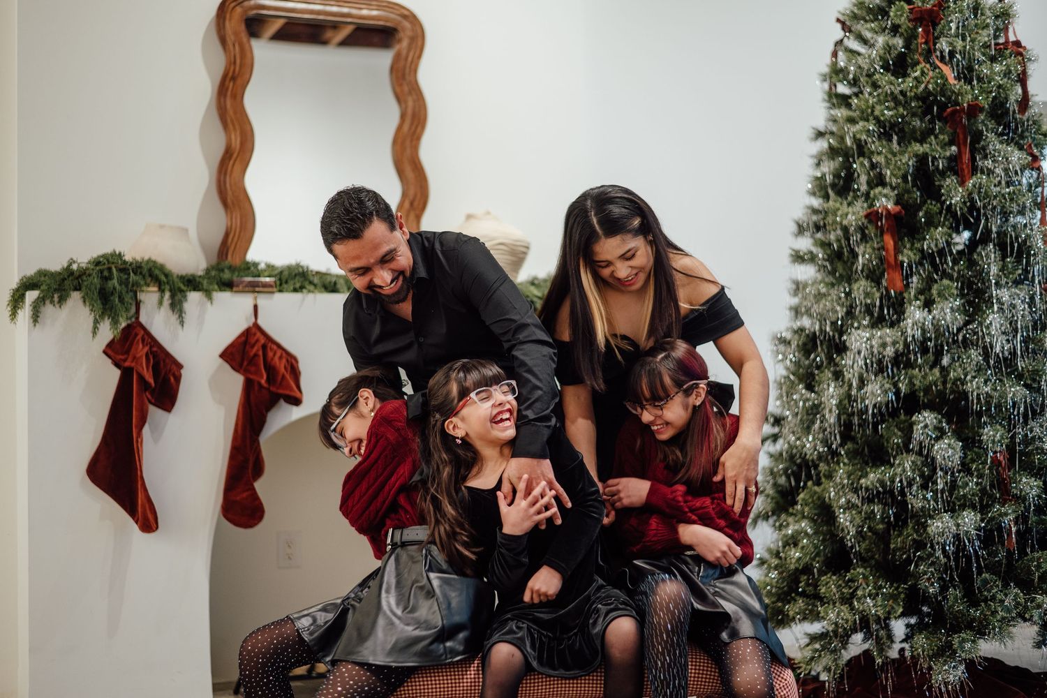A family shares laughter and joy while sitting together near a decorated Christmas tree with stockings hanging on the wall.