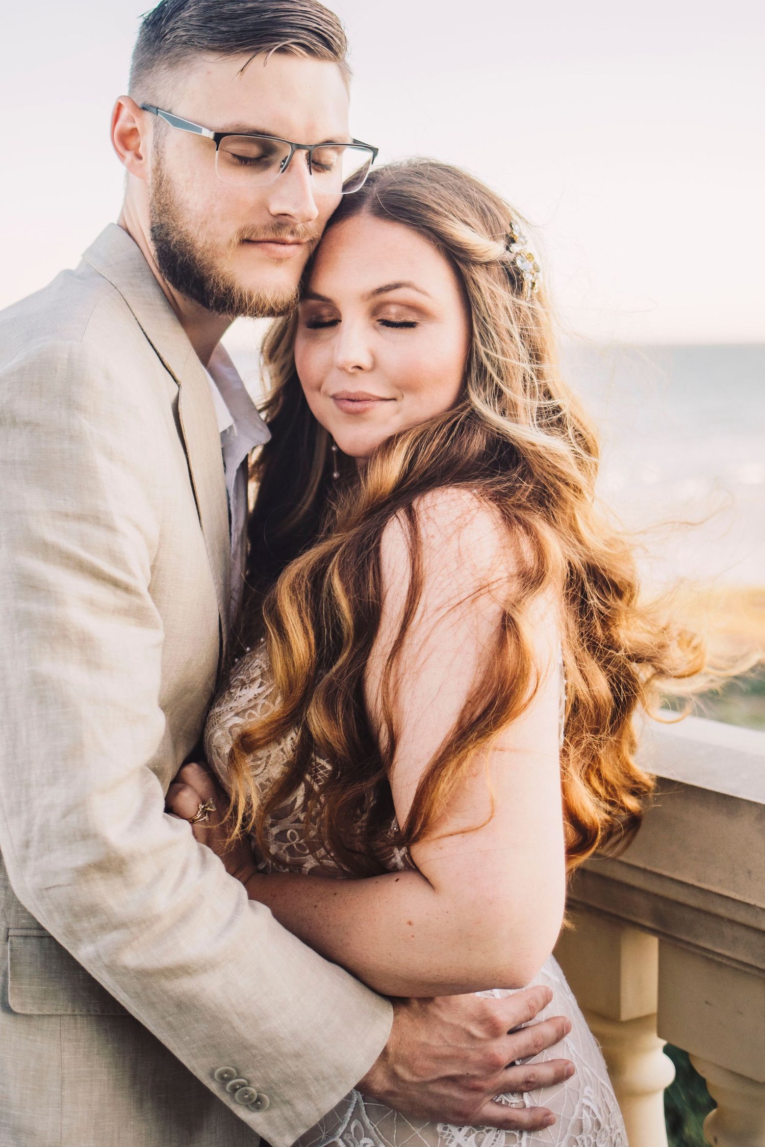 Romantic close-up of bride and groom embracing on seaside balcony at sunset.