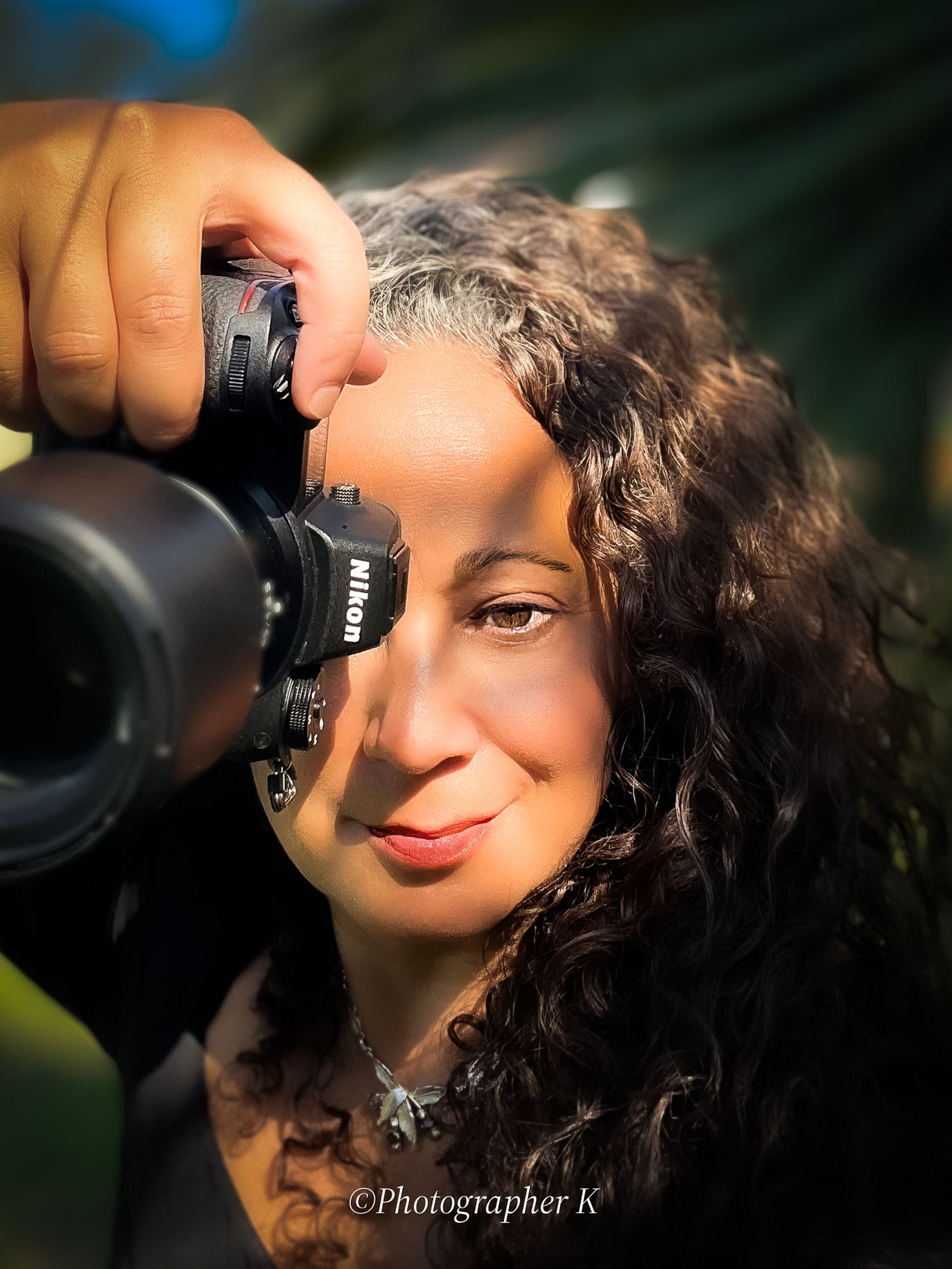 Close-up self portrait of photographer with curly hair taking photo with professional camera.