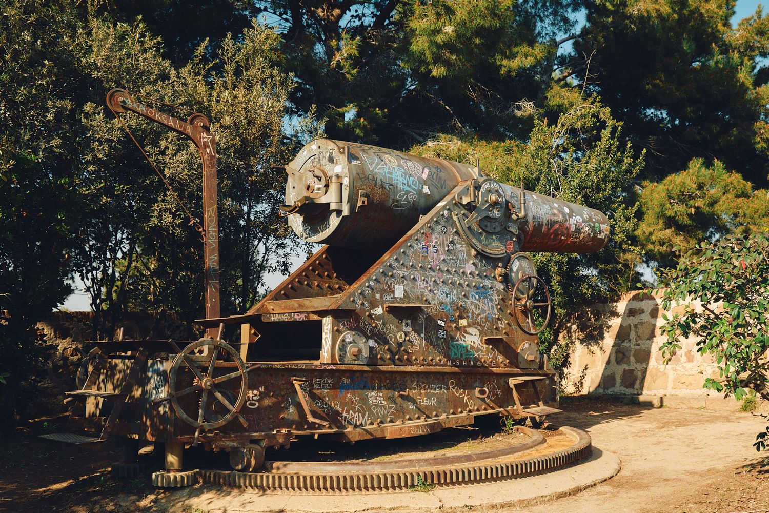 Rusty antique cannon on a rotating platform displayed outdoors among trees, a historic military artifact.
