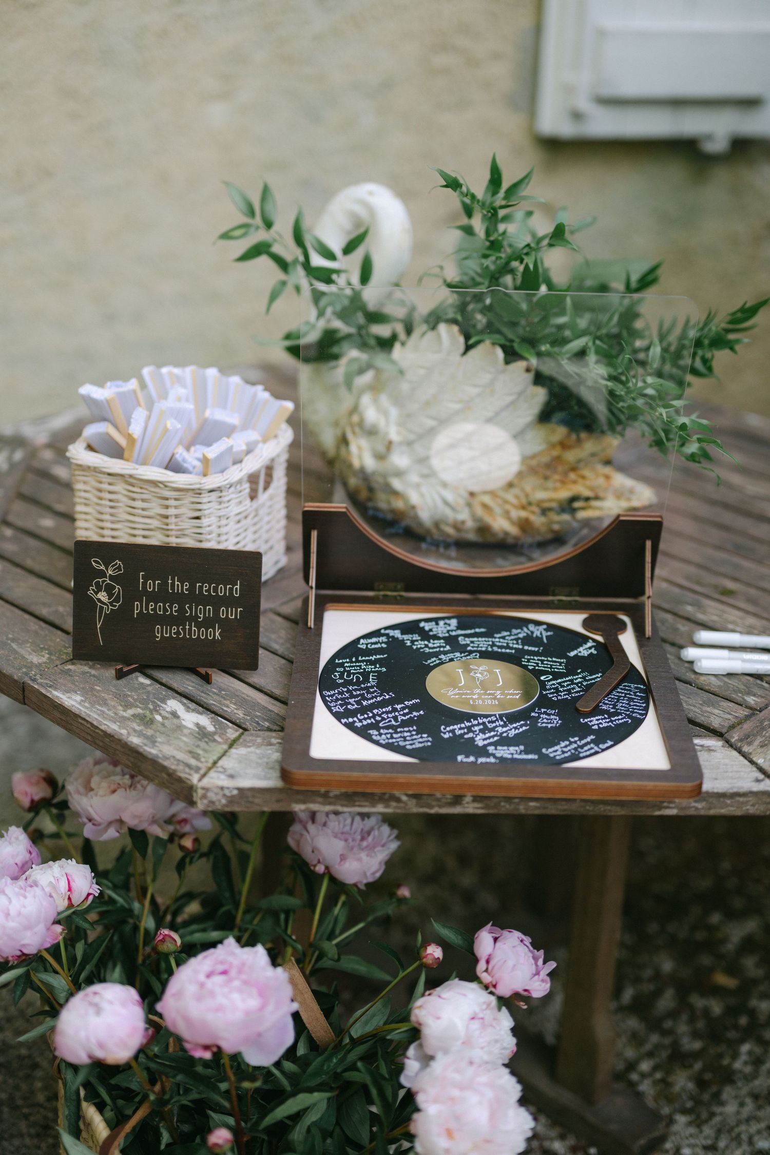 Wedding guestbook vinyl record display on rustic table with pink peonies and swan decoration.