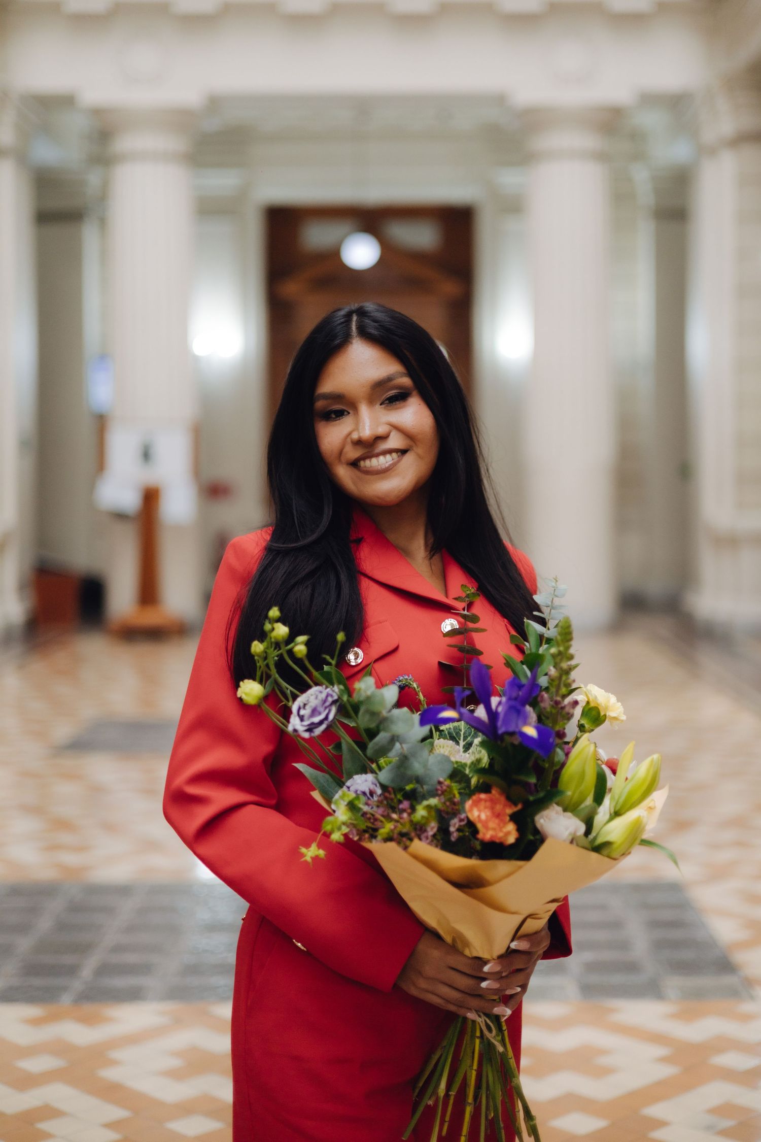 Cheerful woman in red suit holding colorful flower bouquet in elegant interior.
