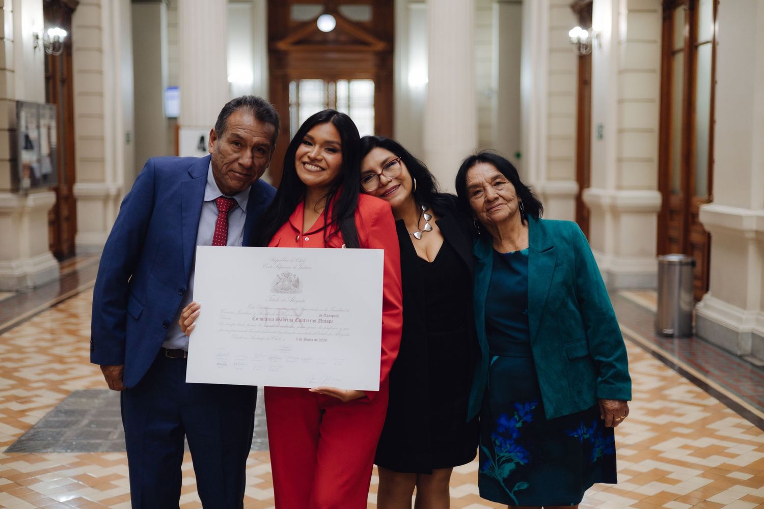 Joyful graduate in red shares celebratory moment with three family members holding diploma.