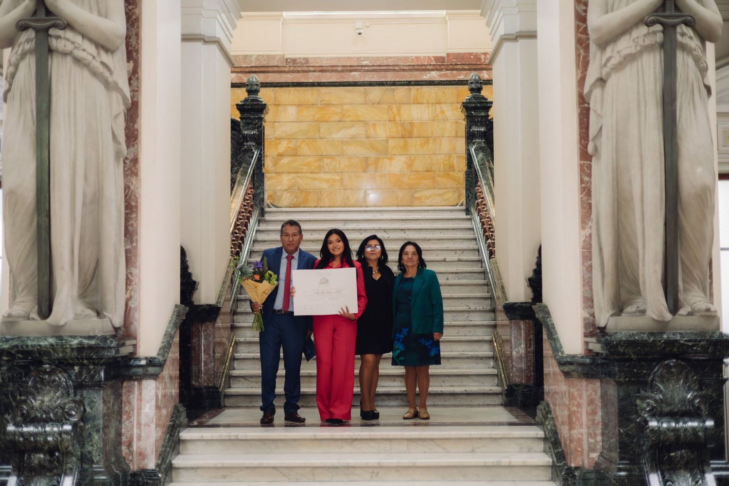 Group of four people pose with certificate on ornate staircase.