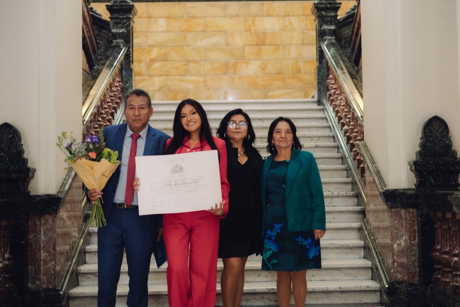 Four people smile holding white certificate on elegant staircase.