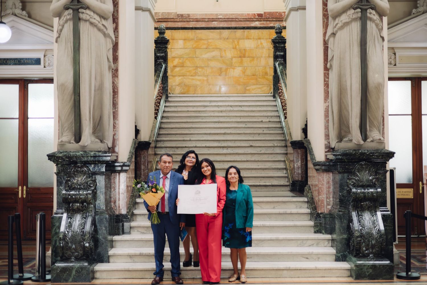 Family group poses with framed certificate on grand marble stairs.