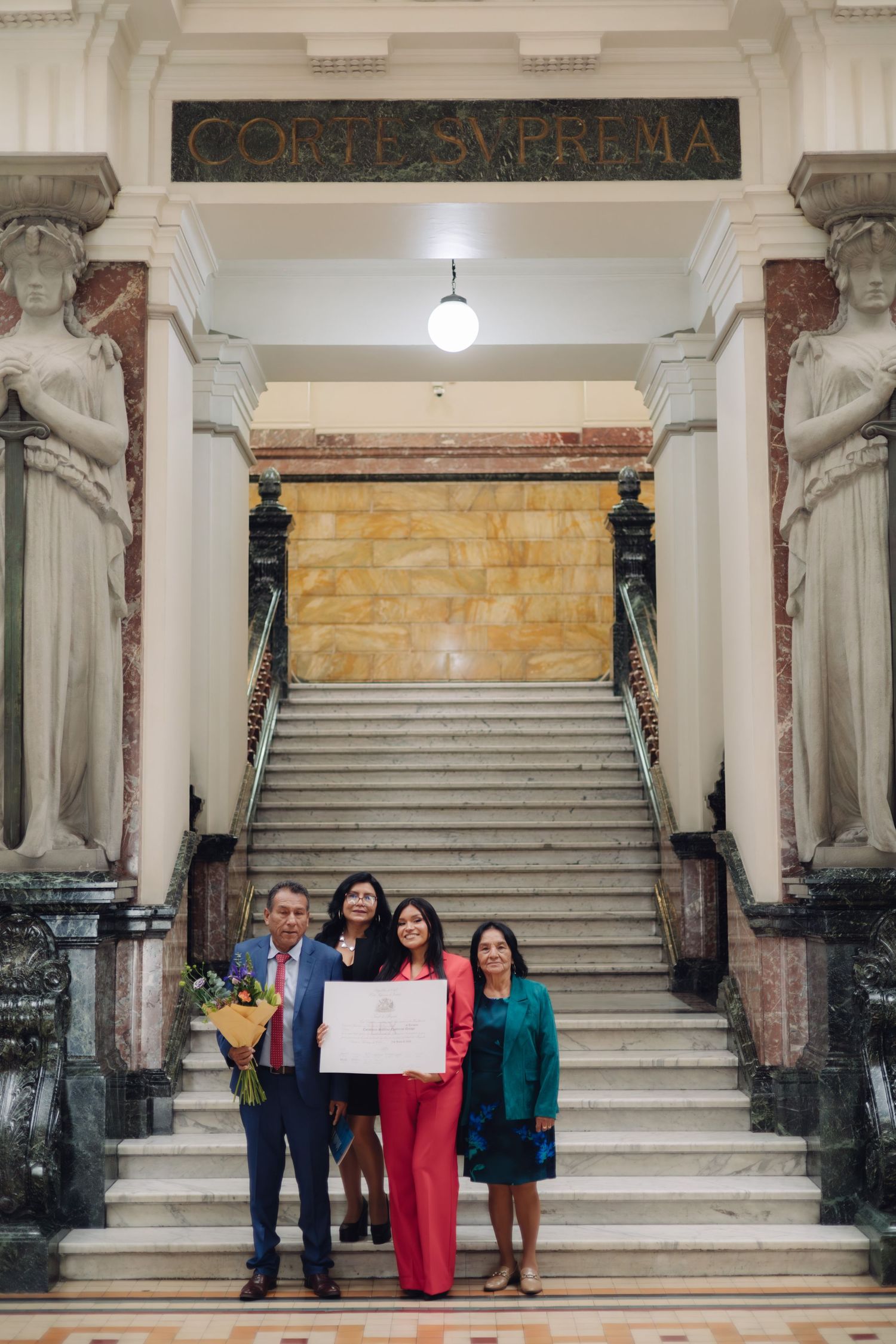 Four people celebrate with certificate at Corte Suprema entrance.