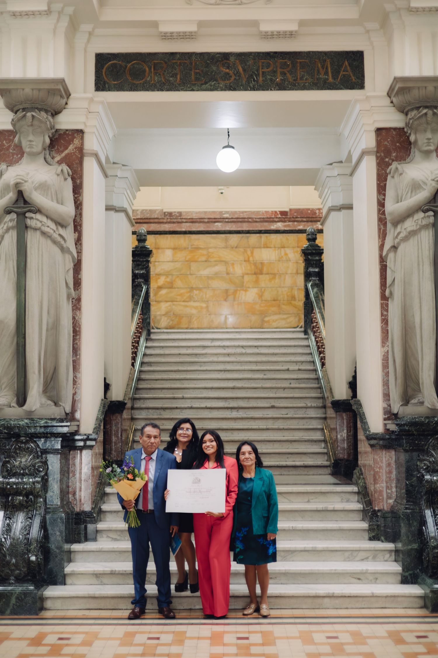 Group holds diploma proudly at Supreme Court marble staircase.