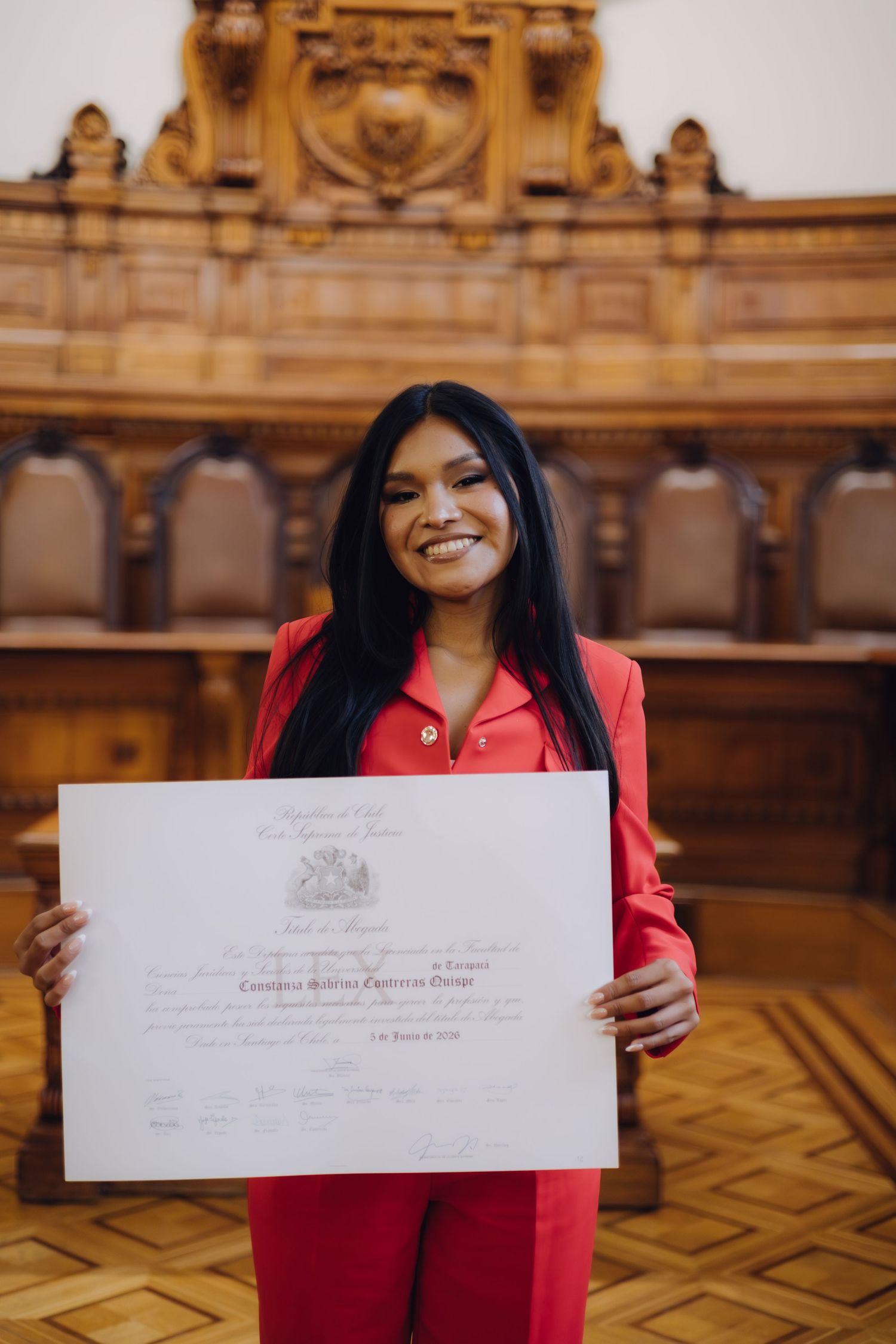 Happy woman in red suit holds Chilean Supreme Court diploma.