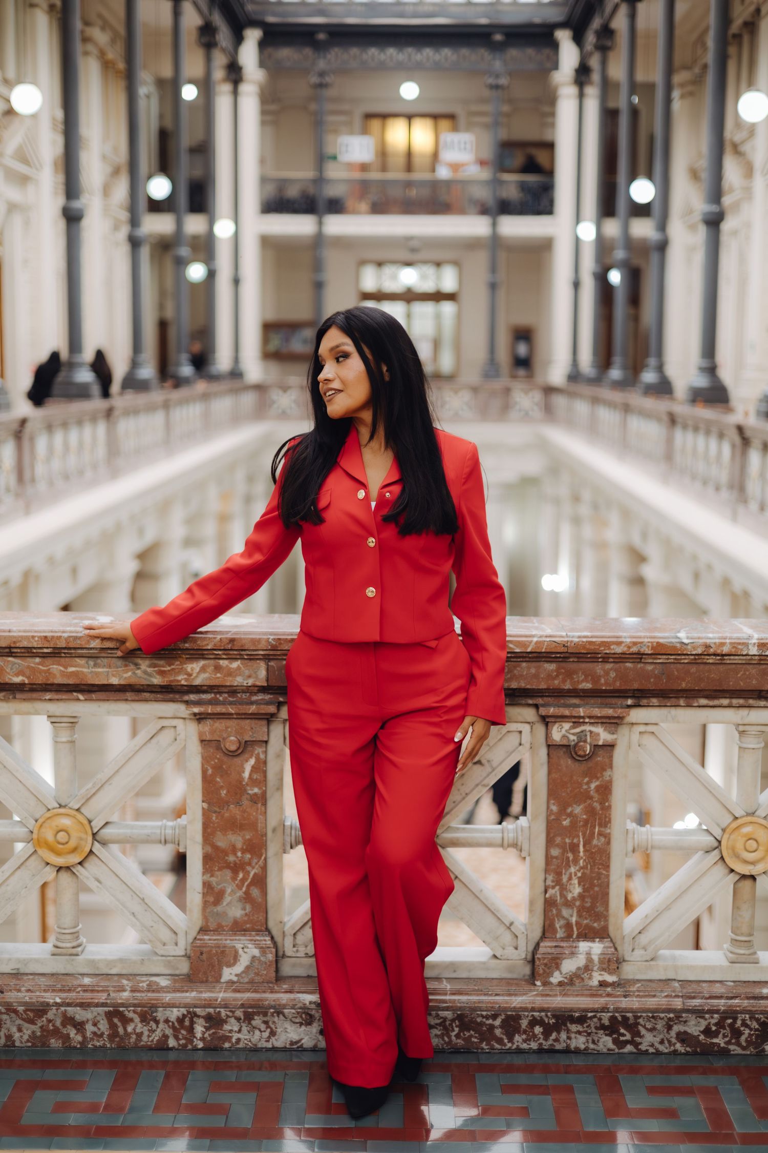 Confident woman in red suit stands in luxurious marble gallery hall.