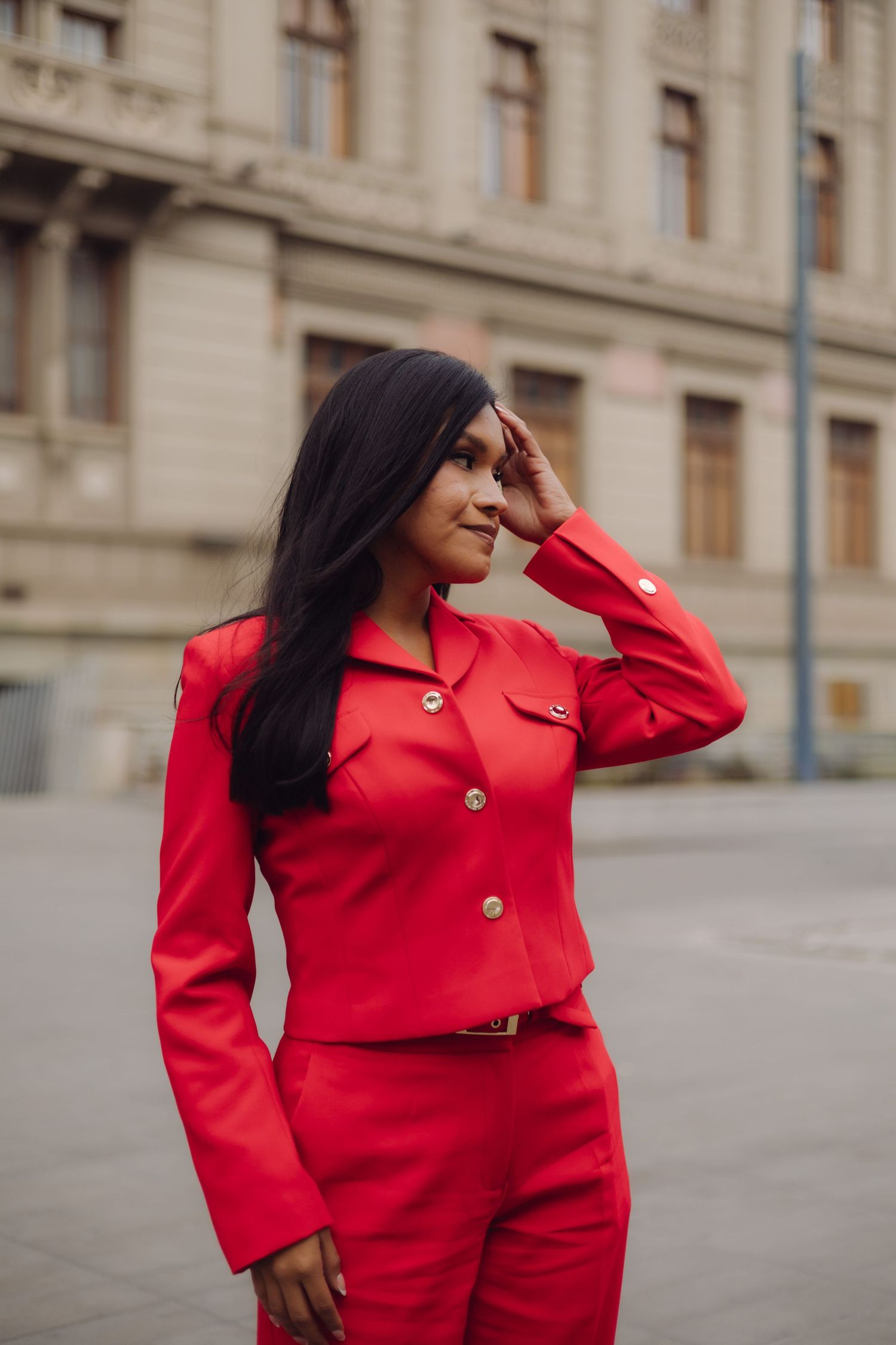 Stylish woman in red cropped jacket and pants posing outdoors near a classic stone building.