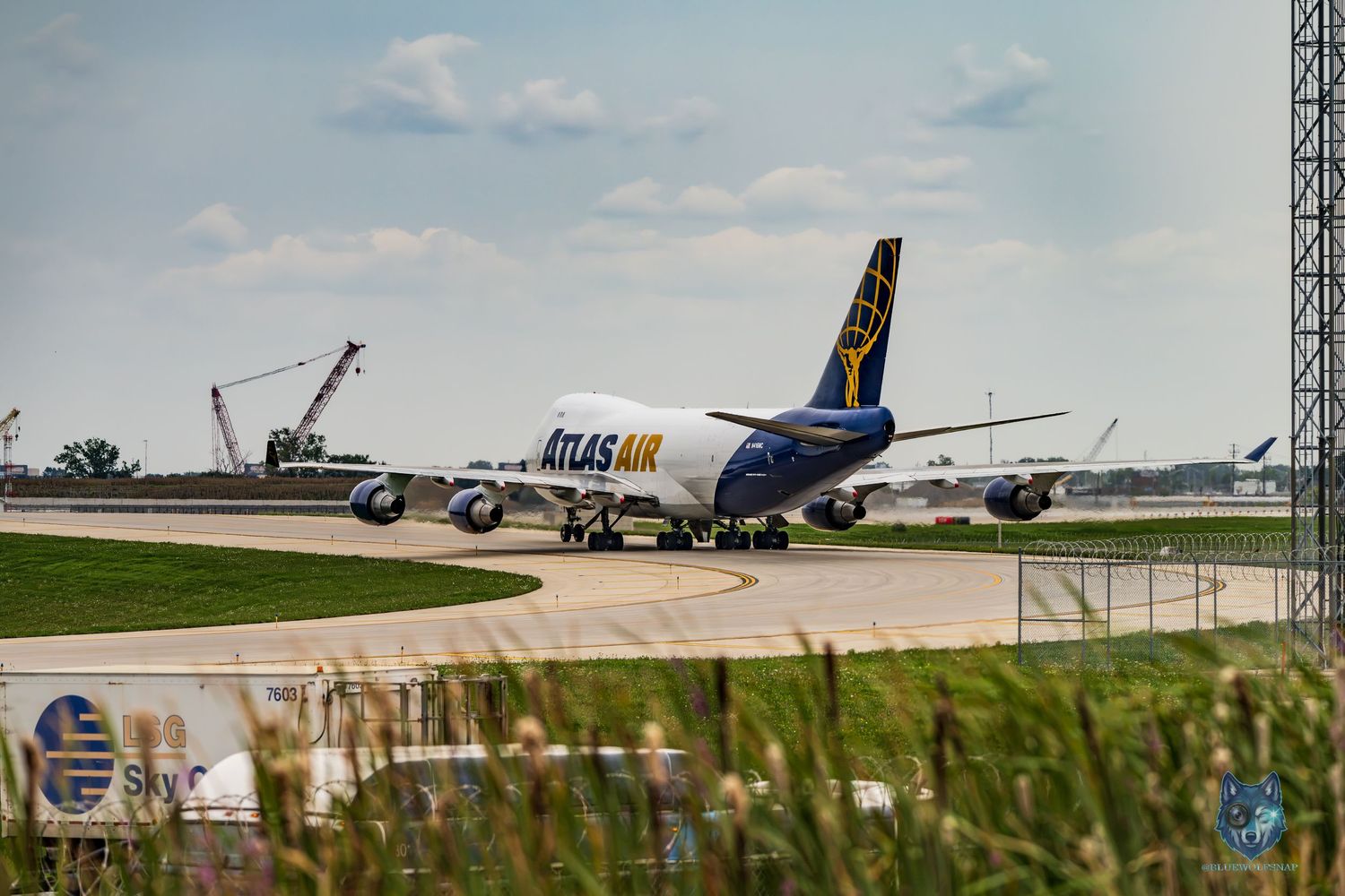 Atlas Air cargo Boeing 747 aircraft taxiing on runway at airport with construction cranes visible in background.
