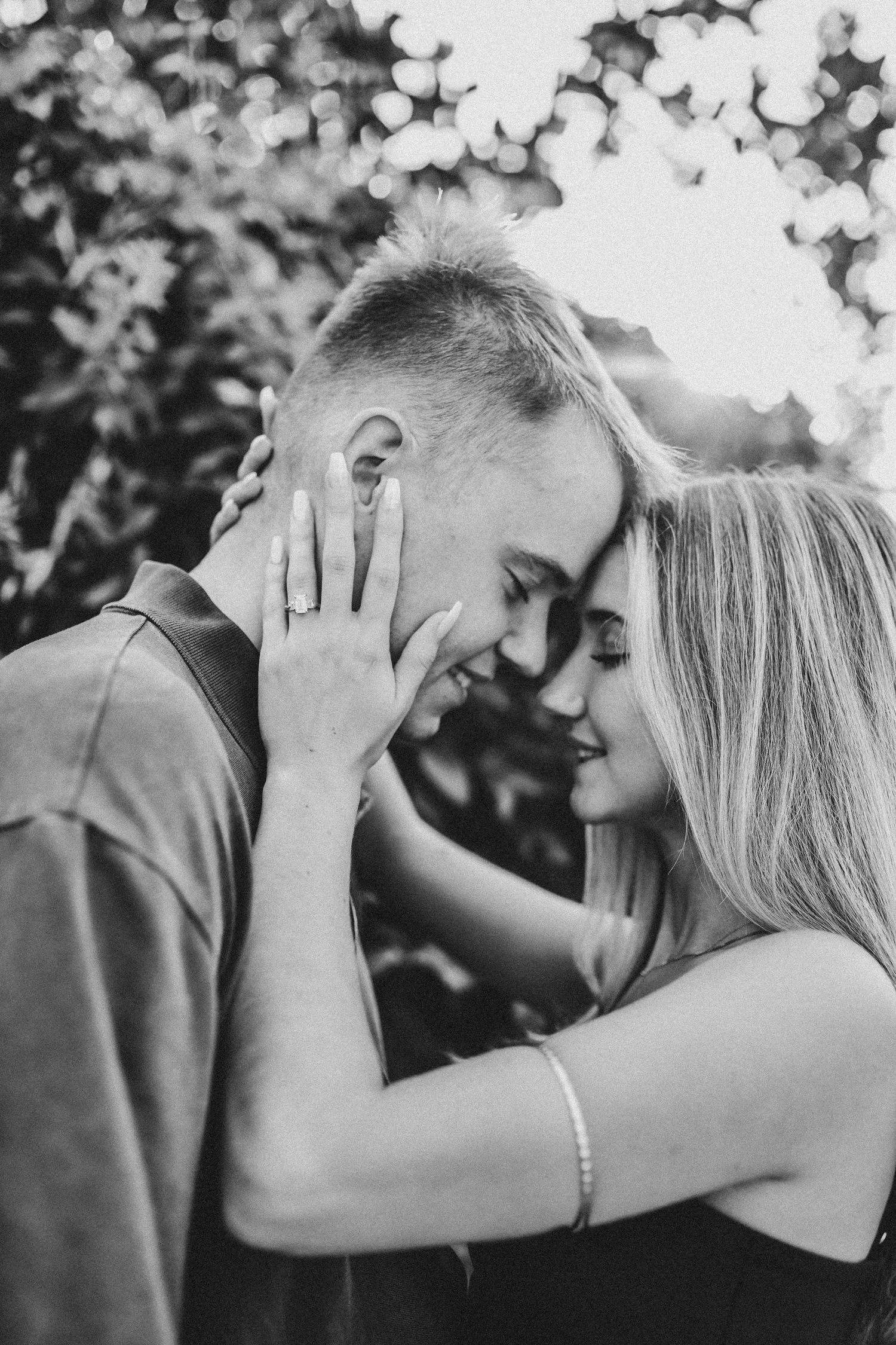 Groom proposing on one knee beneath a beautiful greenery-covered arch