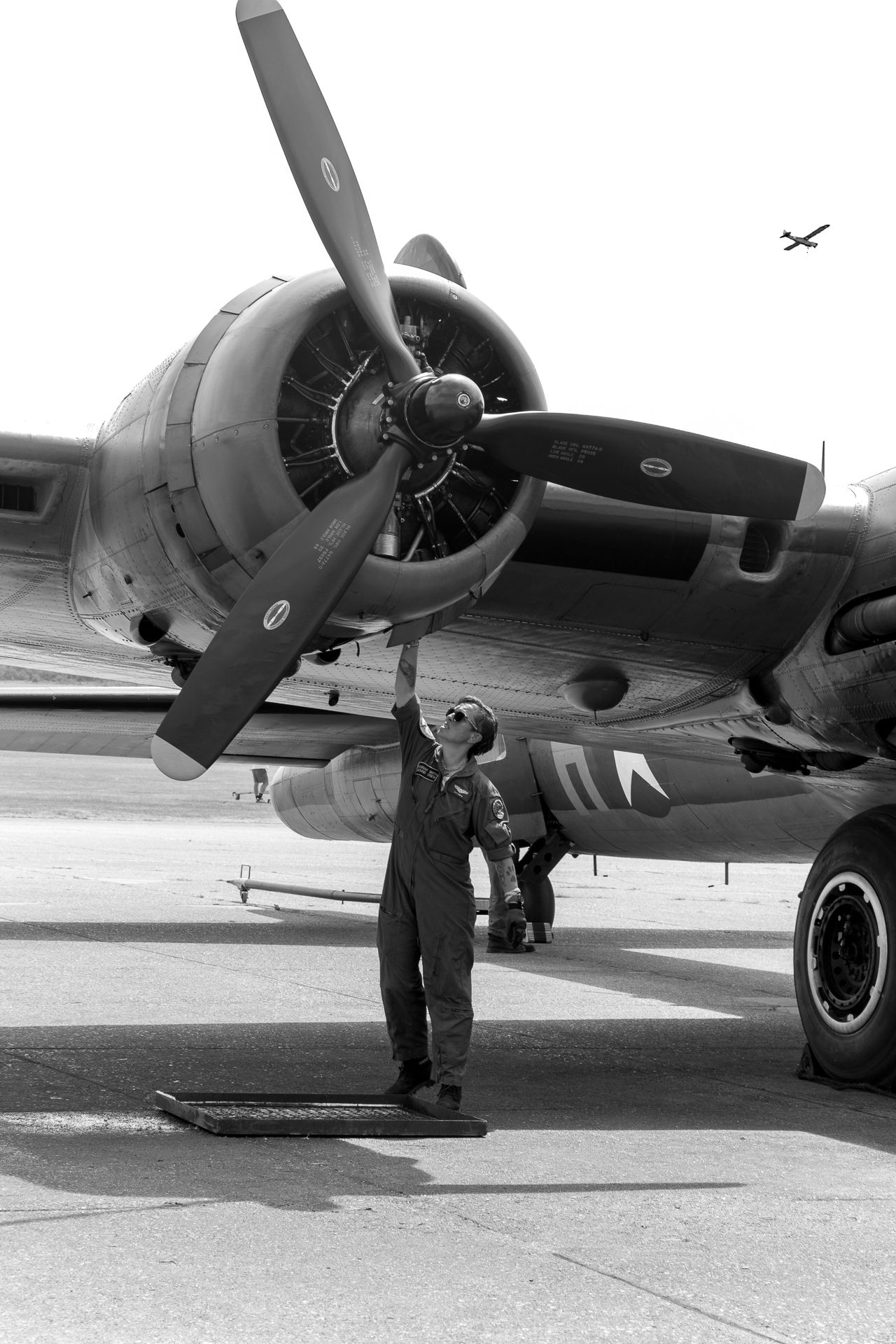 WWII mechanic inspecting B-17 bomber propeller on tarmac, black and white military aviation photograph.