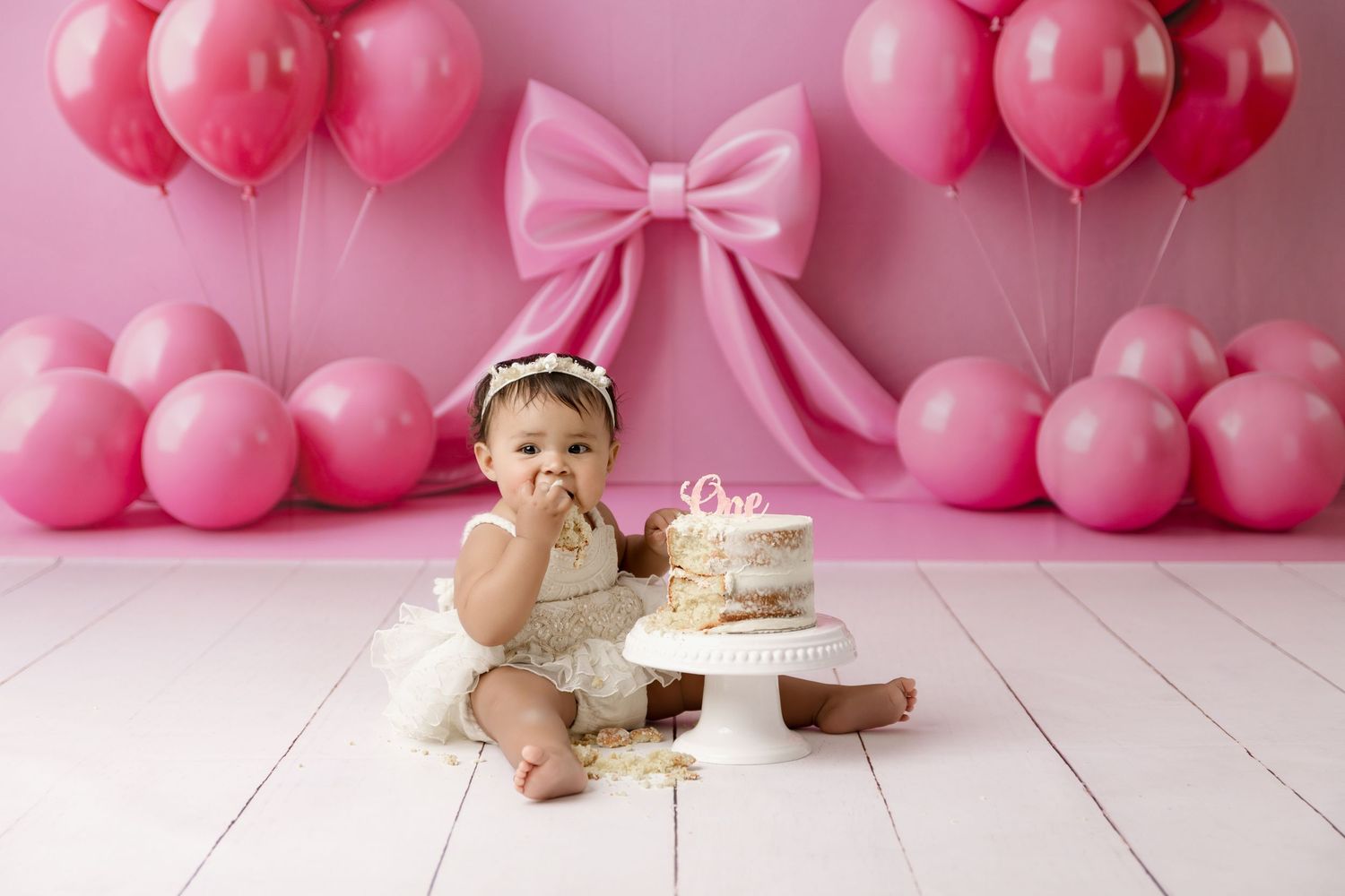 Baby tasting cake beneath a pink balloon and bow backdrop