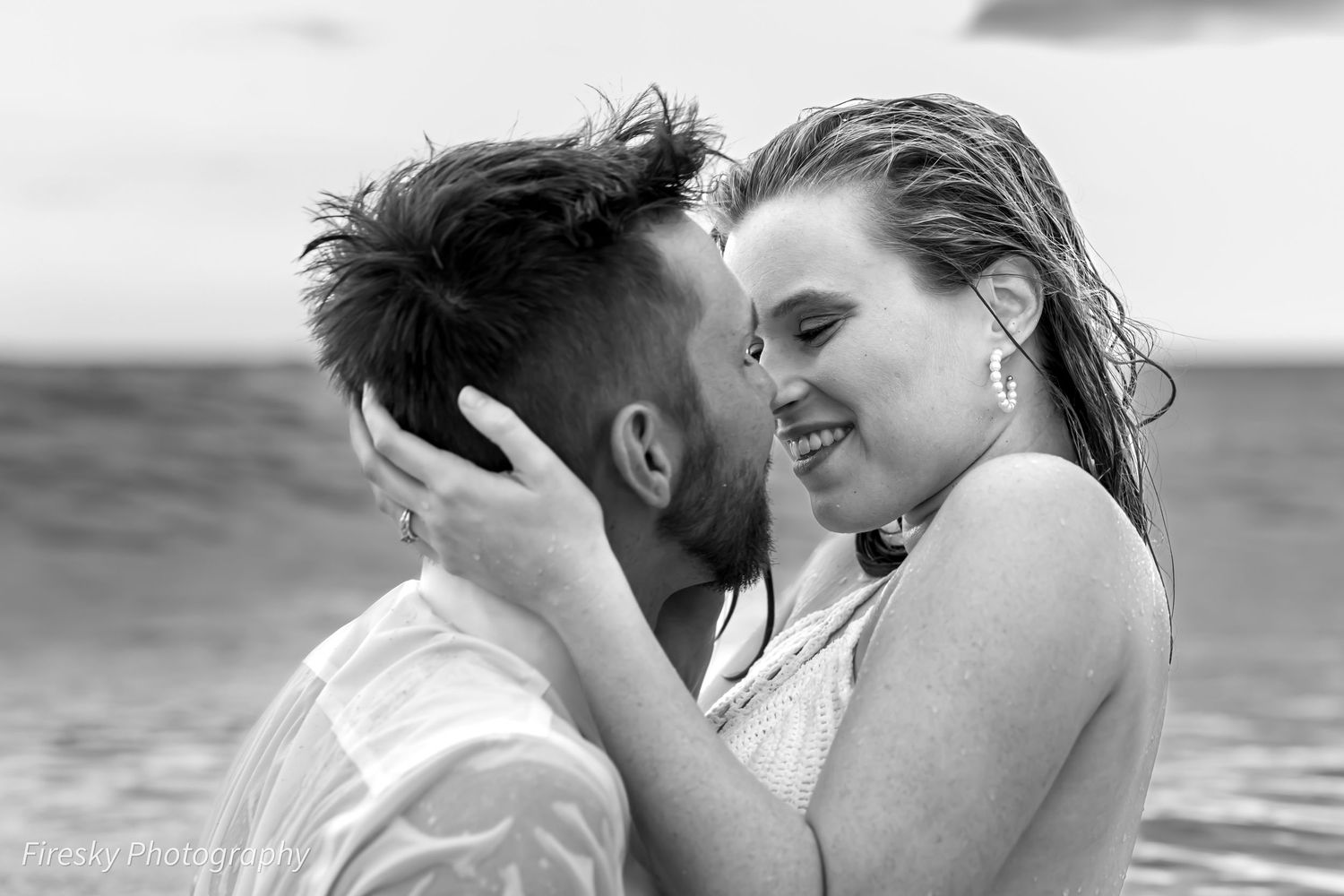 Black and white photo of a couple sharing a romantic moment at the beach, smiling and embracing with wet hair.