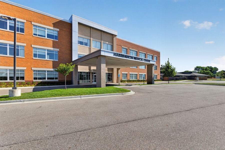 Modern medical center building with brick facade, covered entrance, and spacious parking lot on a sunny day.