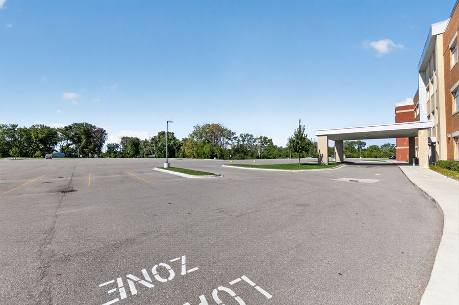 Empty parking lot with a loading zone marking near a brick commercial building surrounded by trees on a clear day.