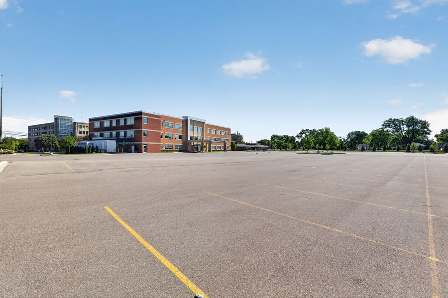 Large empty school parking lot with yellow markings, featuring a modern brick building and trees under a clear blue sky.
